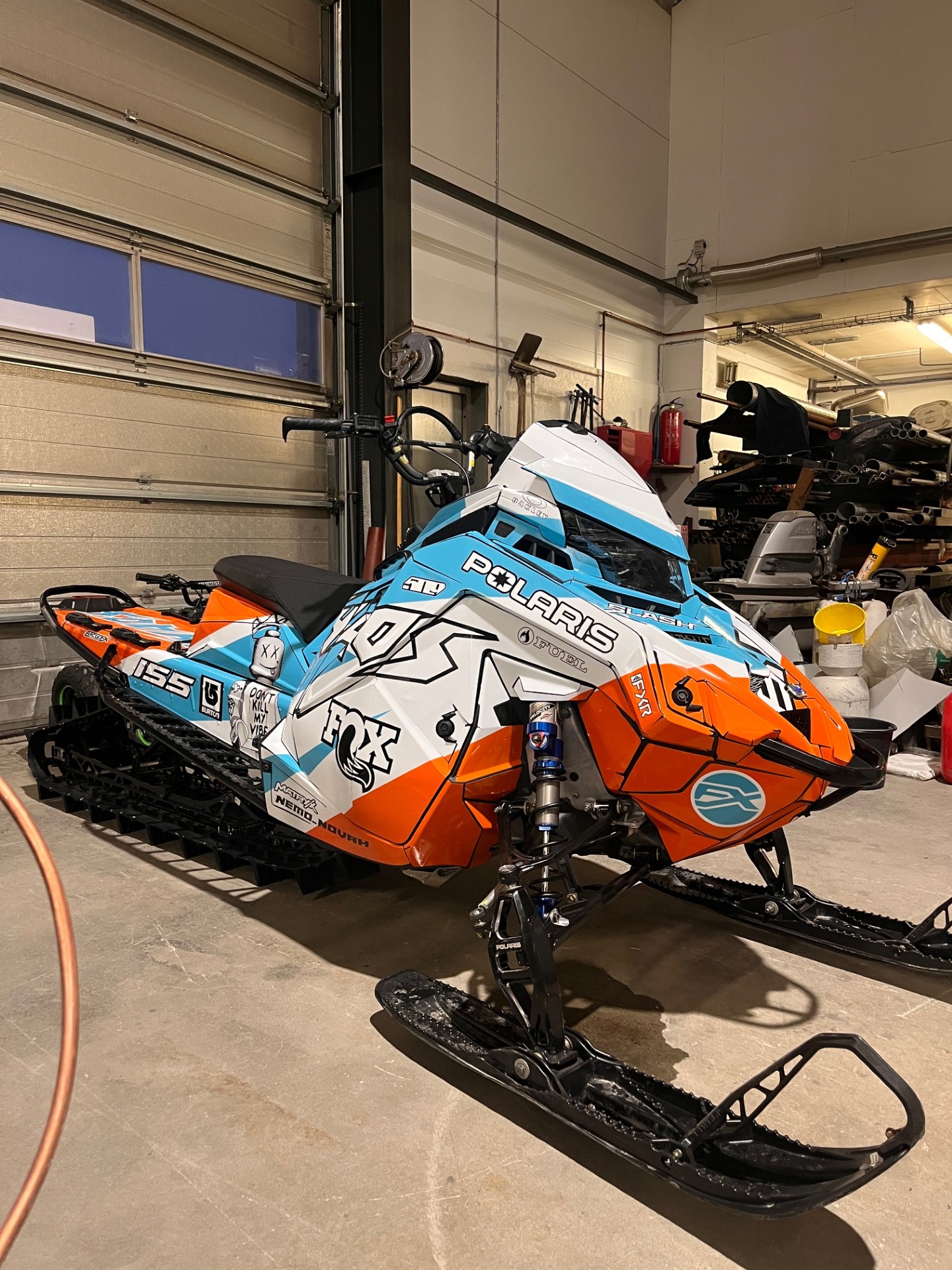 A Polaris Matryx Mountain snowmobile with a white, black, ice blue, orange, and axys burst Curtis Ascent custom vinyl wrap.