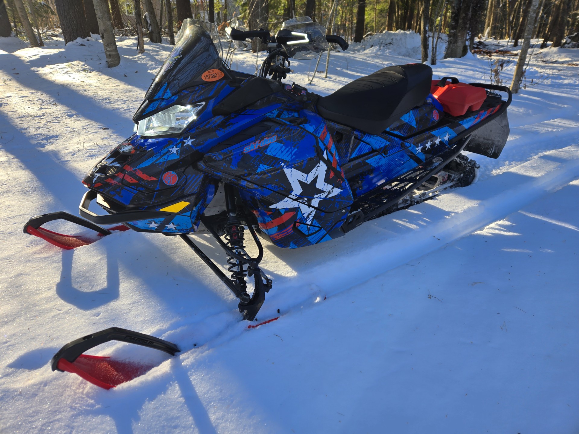 A Ski-Doo Gen4 Wide Body snowmobile with a octane blue, lava red,gunmetall gray, and white Wartorn custom vinyl wrap.