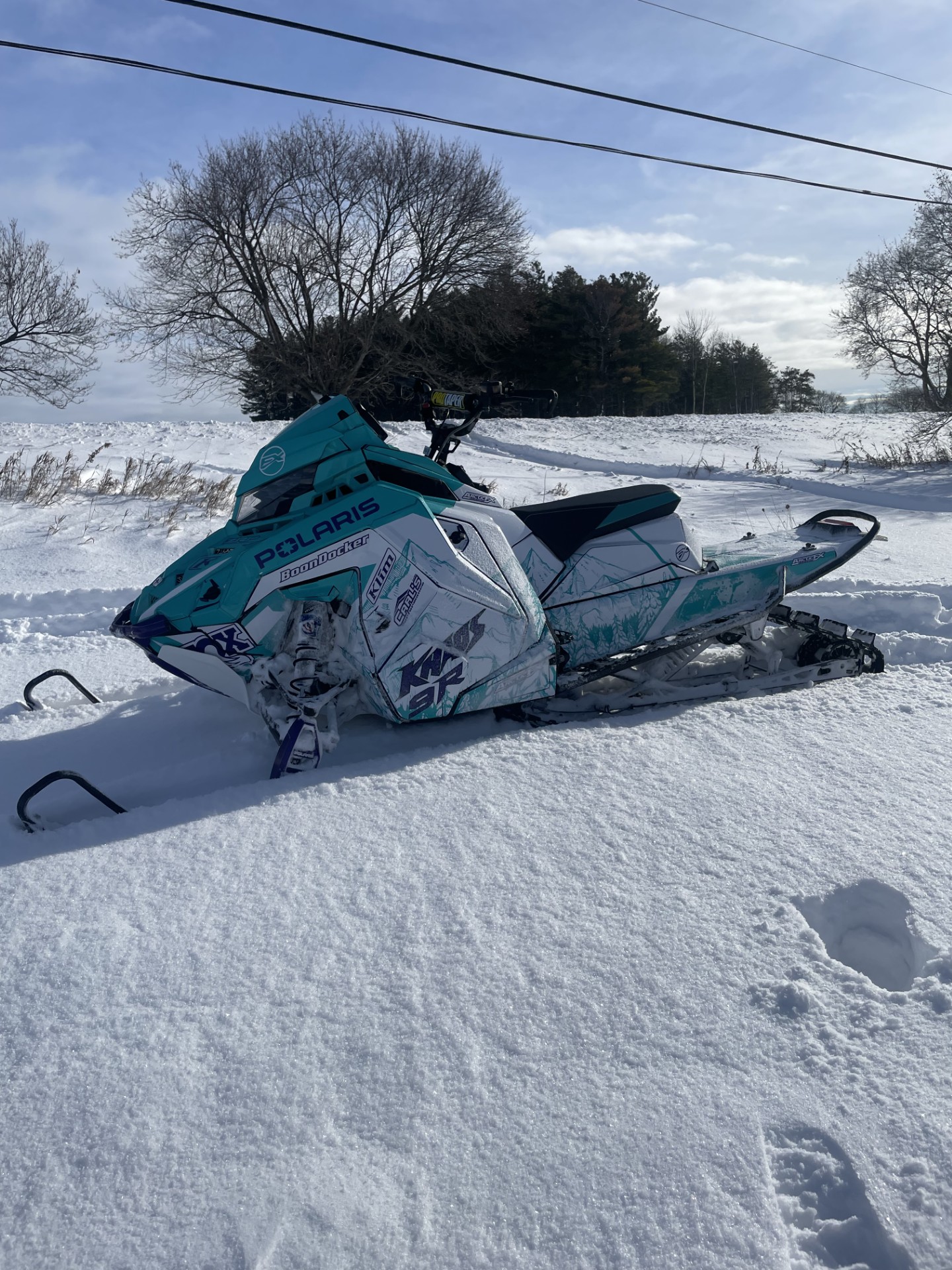 A Polaris Matryx Mountain snowmobile with a khaos purple, white, and radiant green Andy Thomas Peaked custom vinyl wrap with silver flake laminate.
