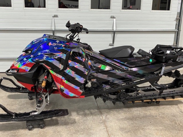 A Lynx snowmobile with a white, black, monument gray, polar blue, Polaris red Electro custom vinyl wrap with prismatic chrome.