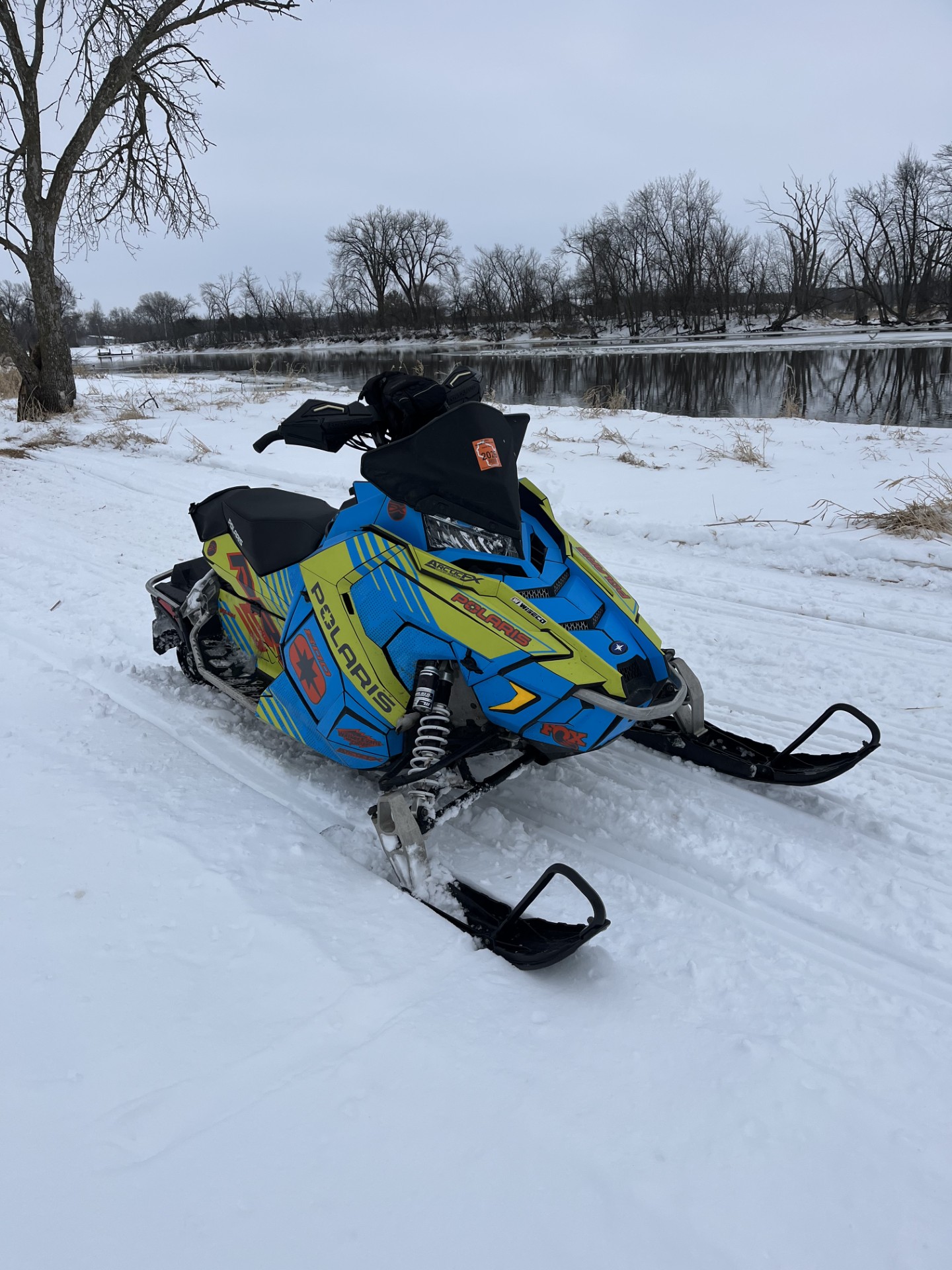 A Polaris Axys Trail snowmobile with an axys burst, asphalt gray, octane blue, ghost gray, and manta green Armada custom vinyl wrap with matte laminate.