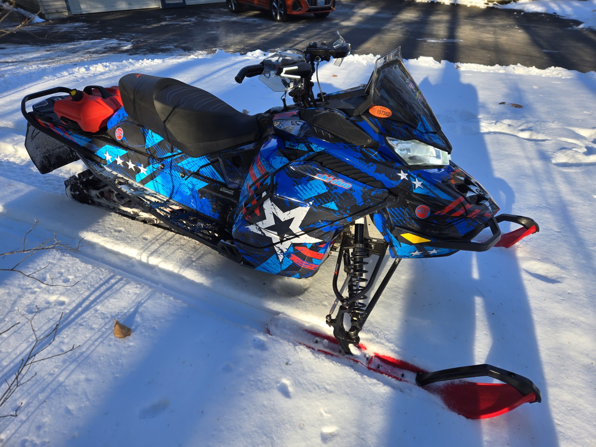 A Ski-Doo Gen4 Wide Body snowmobile with a octane blue, lava red,gunmetall gray, and white Wartorn custom vinyl wrap.