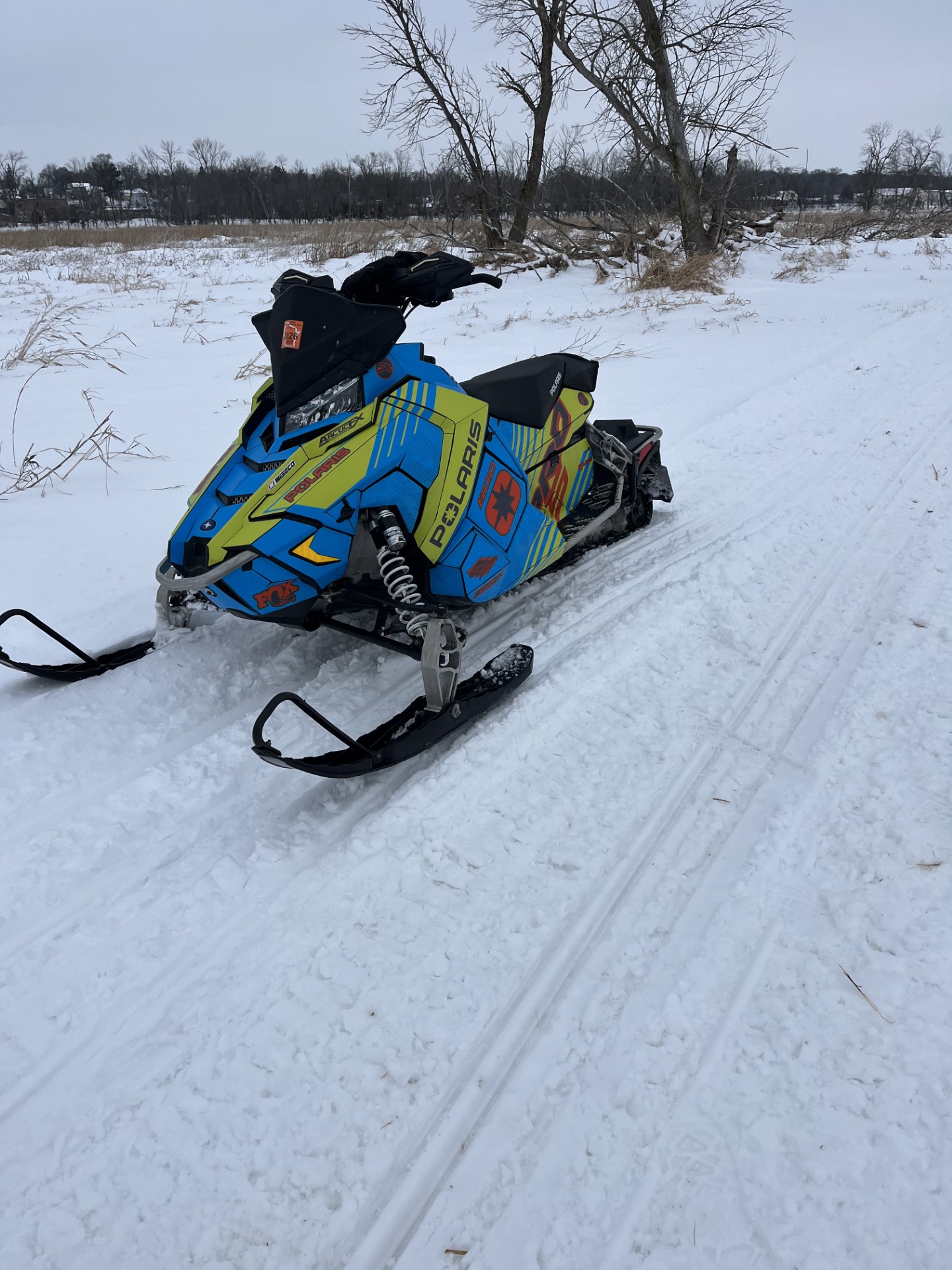 A Polaris Axys Trail snowmobile with an axys burst, asphalt gray, octane blue, ghost gray, and manta green Armada custom vinyl wrap with matte laminate.
