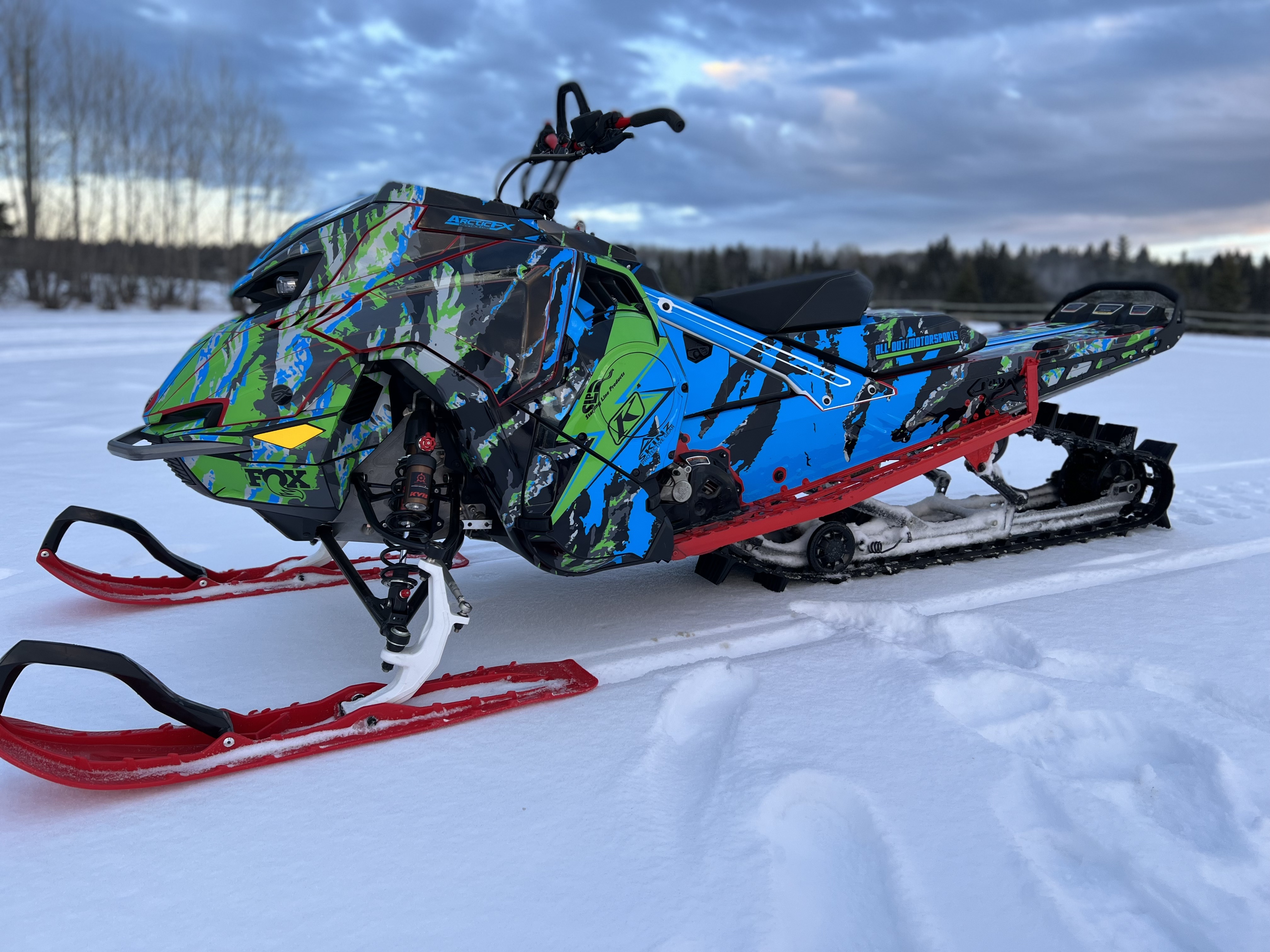 A Lynx snowmobile with an octane blue, black, asphalt gray, sky blue, light gray, and electric green Adams Inversion custom vinyl wrap. 