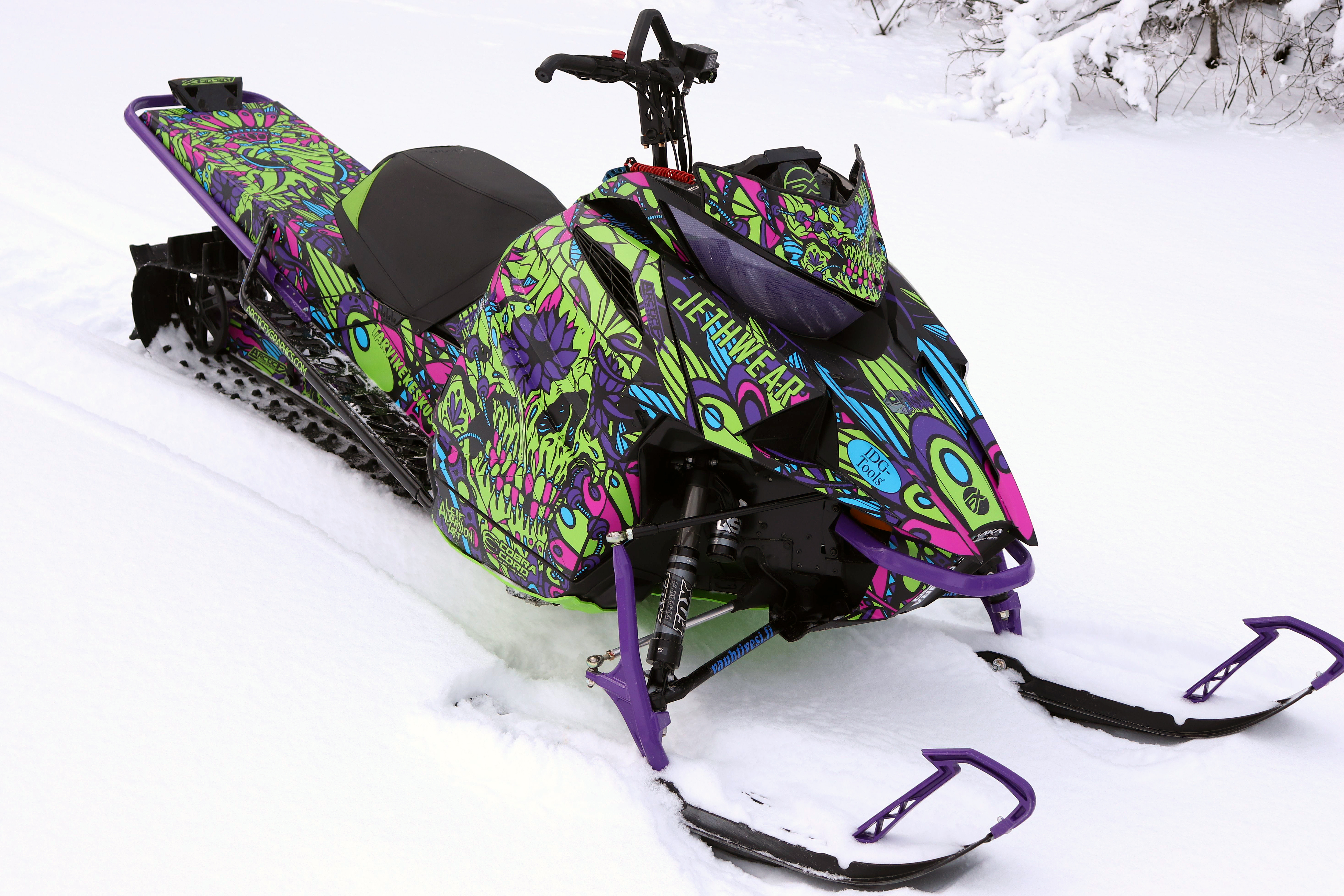 A Arctic Cat Ascender snowmobile with a green, purple, and blue sugar skull Leif Alvarsson Calavera custom vinyl wrap.