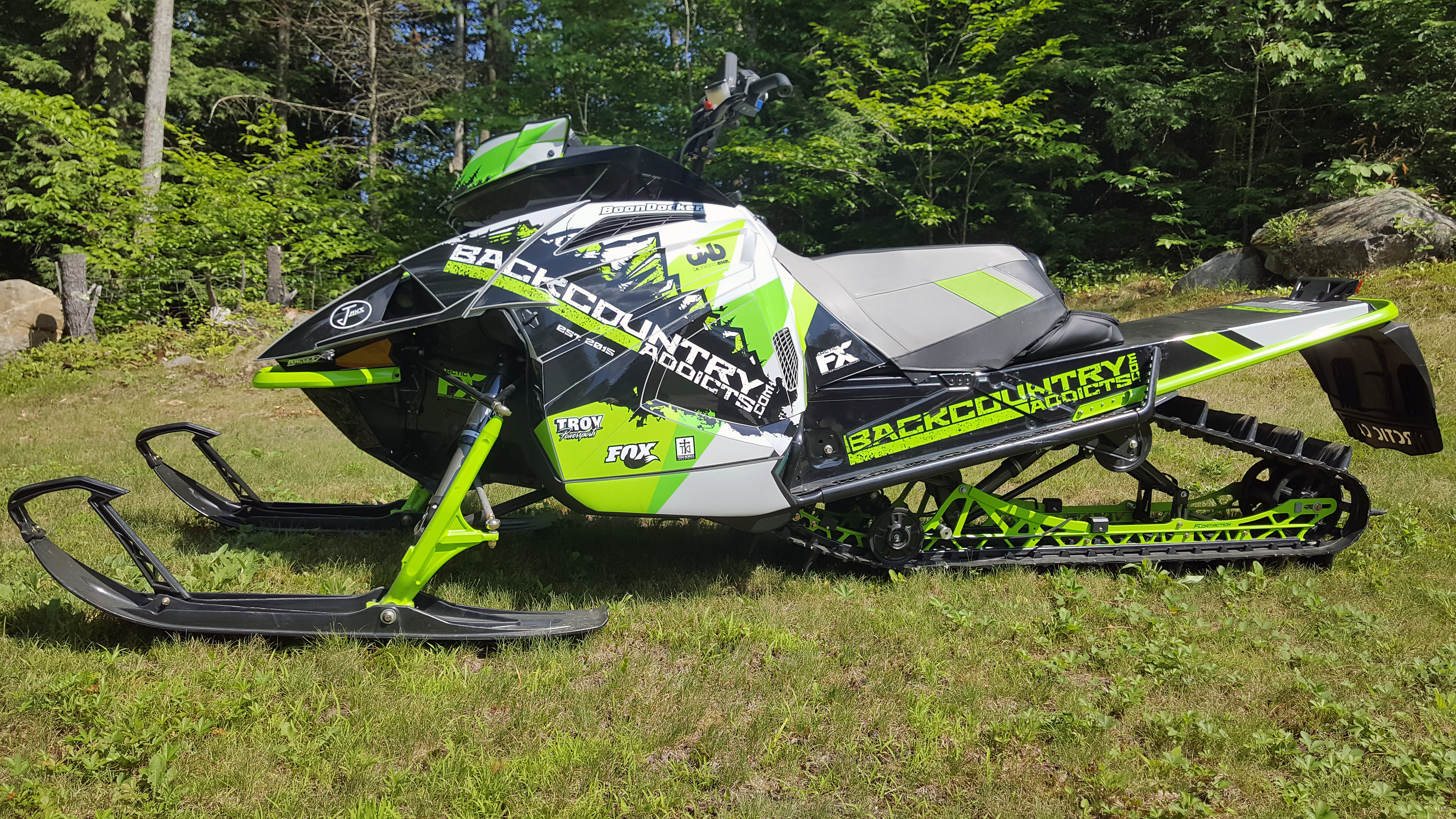 A Arctic Cat Ascender snowmobile with a green, gray, and black grunge mountain backcountry custom vinyl wrap.