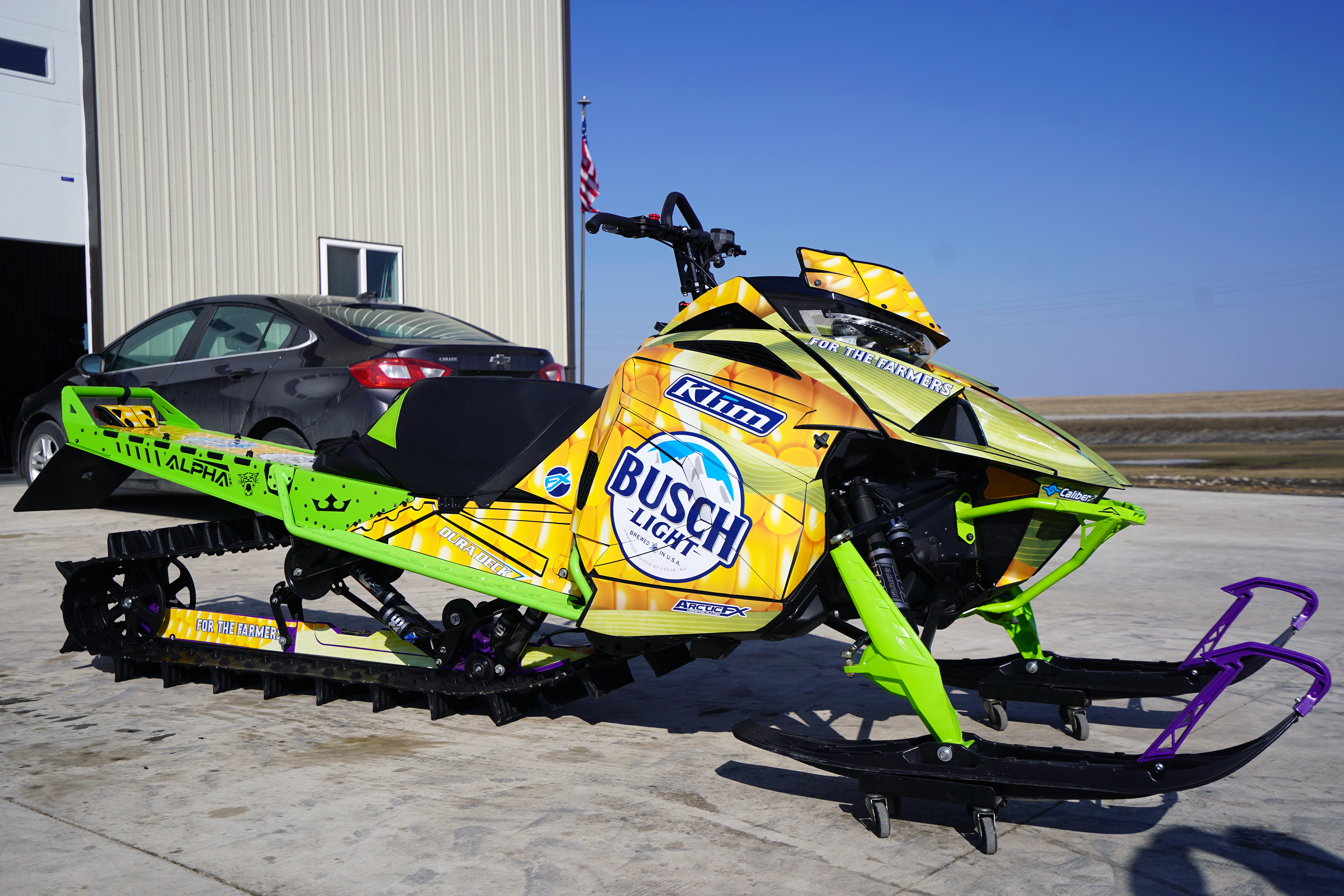 A Arctic Cat Ascender snowmobile with a green and yellow corn farmers Busch Light custom vinyl wrap.