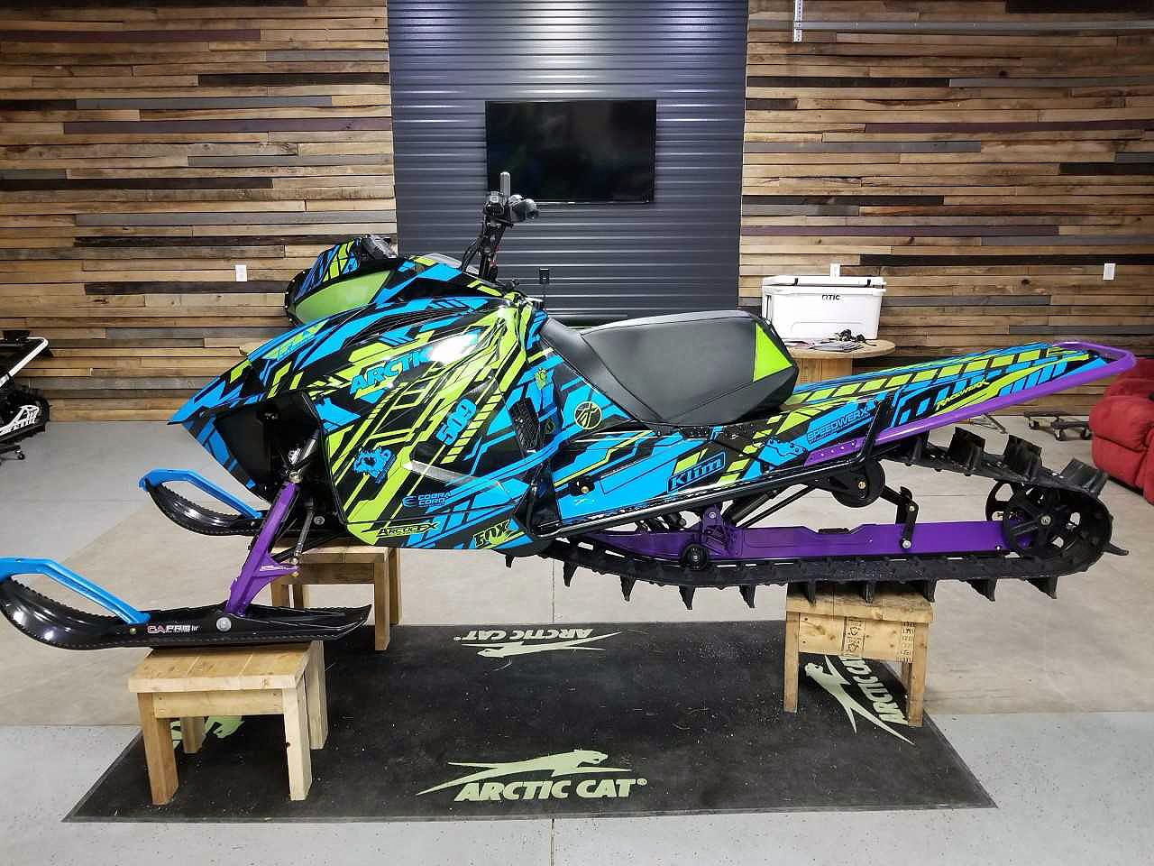 A Arctic Cat Ascender snowmobile with a blue, lime, and black stripes Evasion custom vinyl wrap.