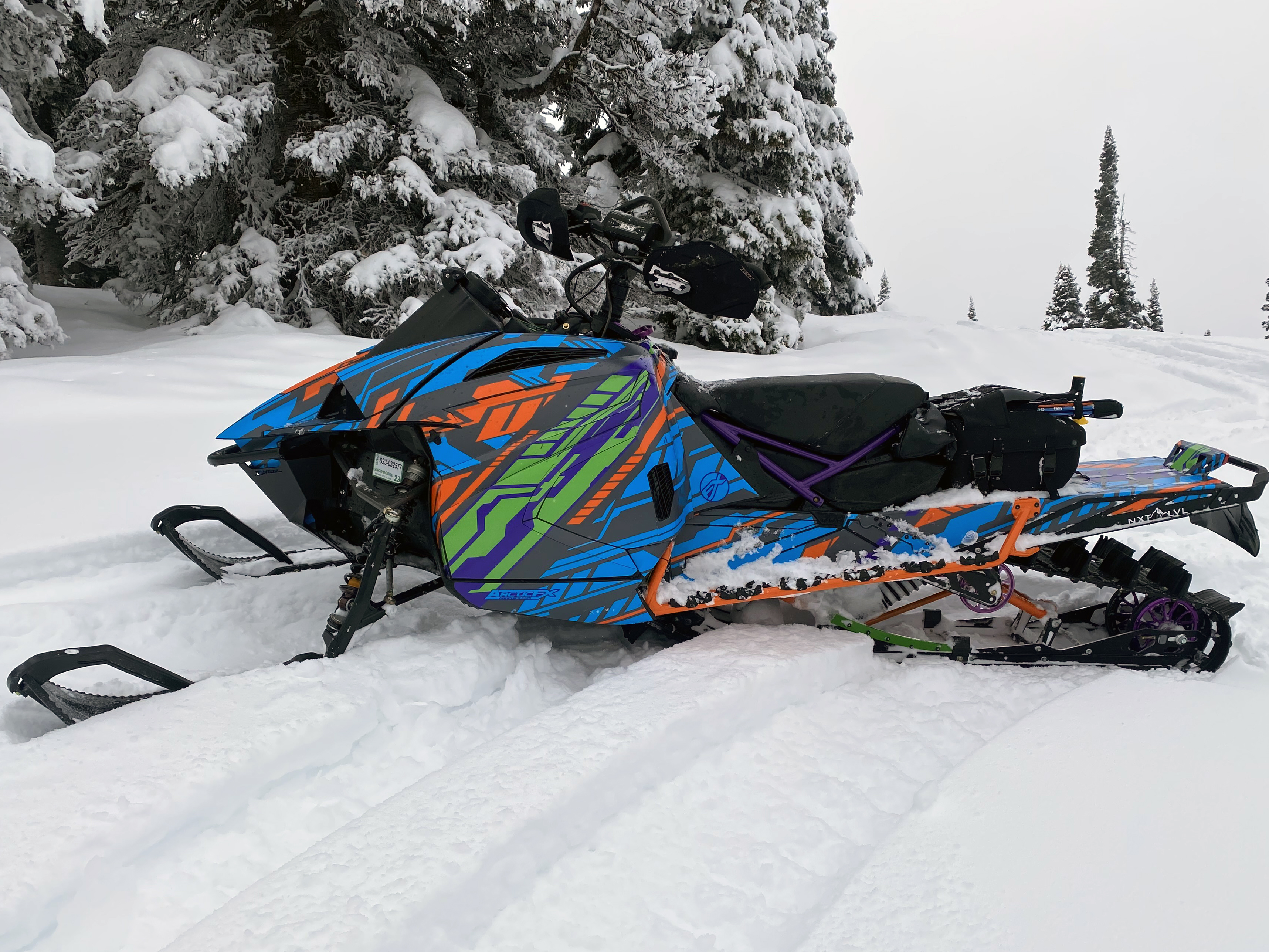 A Arctic Cat Ascender snowmobile with a green, gray, blue, and orange Evasion custom vinyl wrap.
