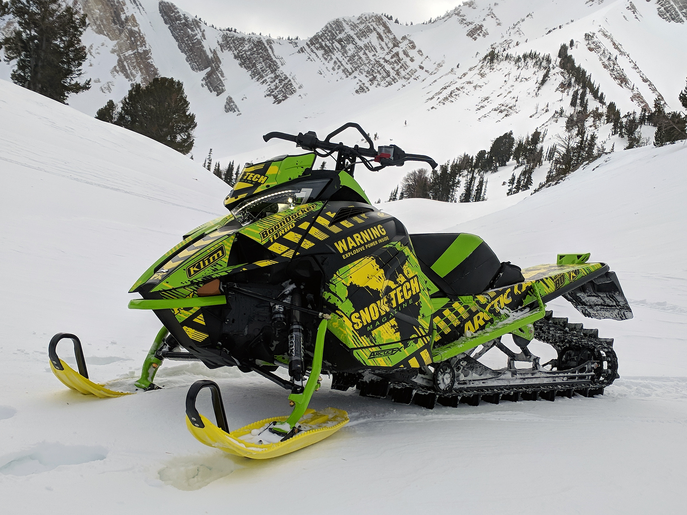 A Arctic Cat Ascender snowmobile with a green, yellow, and black toxic grunge SnowTech custom vinyl wrap.