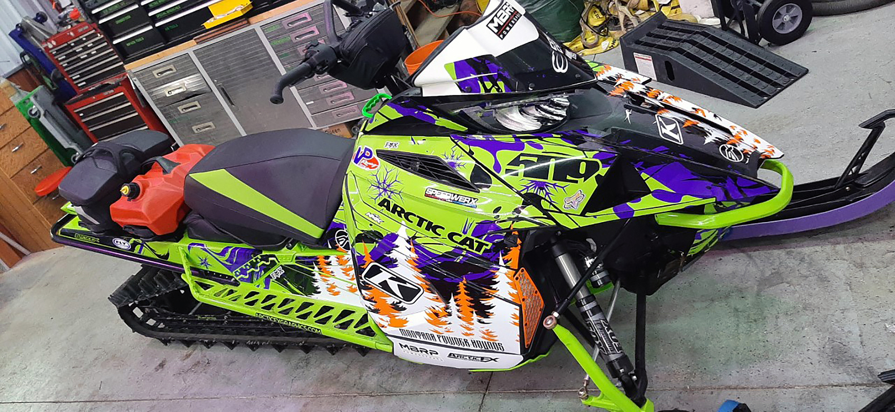 A Arctic Cat Ascender snowmobile with a green, purple, and orange Sub Zero custom vinyl wrap.