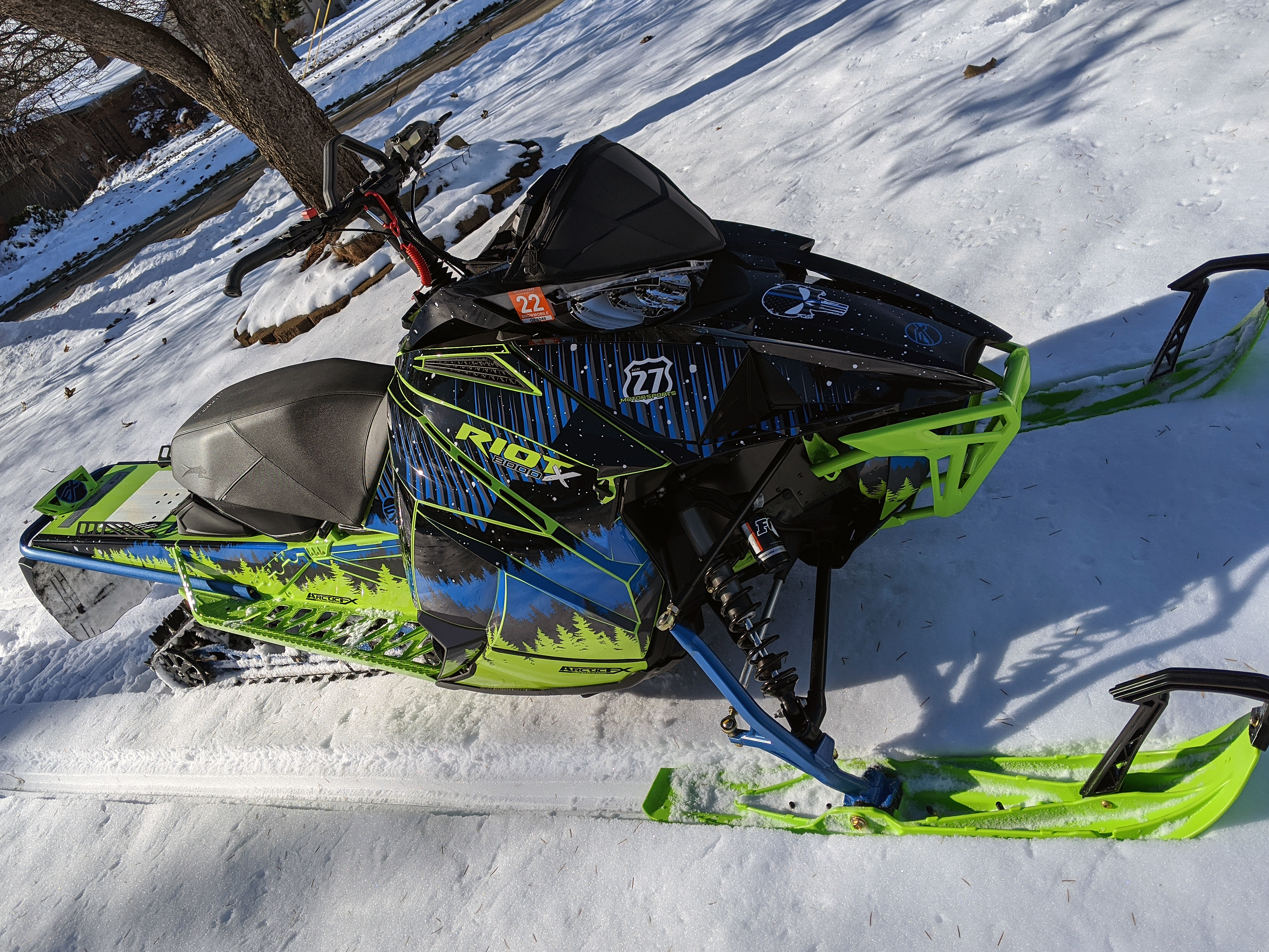 A Arctic Cat Next-Gen snowmobile with a green, blue, and black mountain Aurora custom vinyl wrap.
