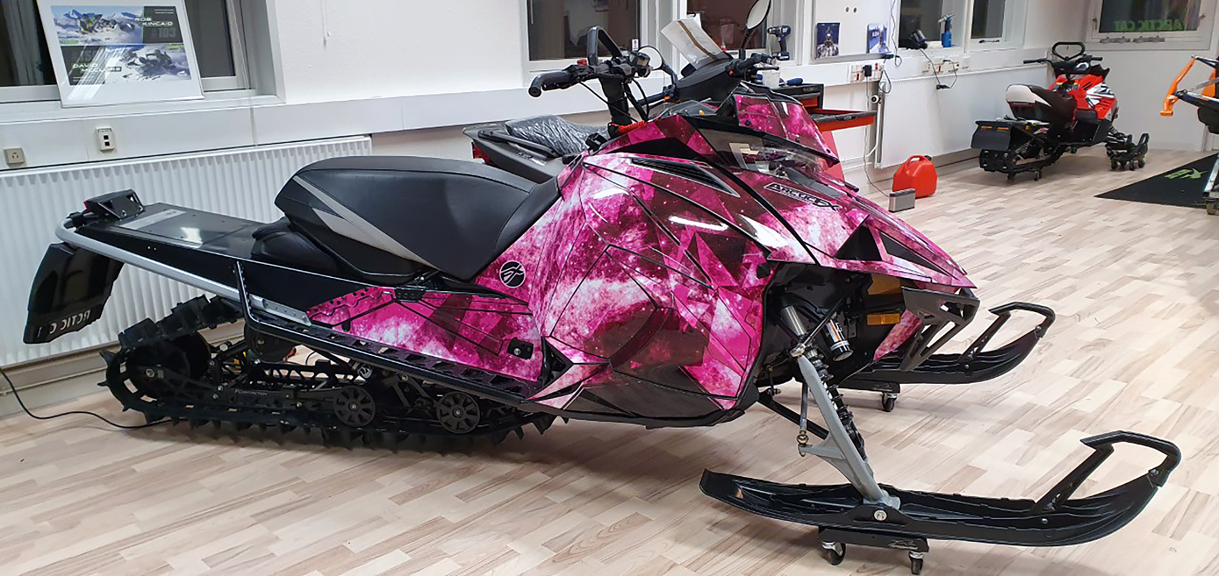 A Arctic Cat Next-Gen snowmobile with a pink and black Cosmic Camo galaxy custom vinyl wrap.