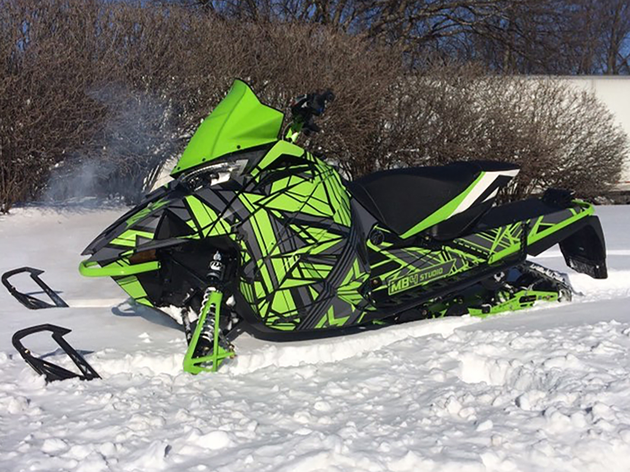 A Arctic Cat Next-Gen snowmobile with a black, gray, and green MB4 Mayhem custom vinyl wrap.