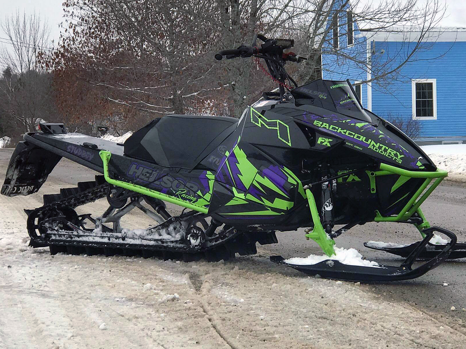 A Arctic Cat Proclimb snowmobile with a purple, green, and black grunge mountain Altitude custom vinyl wrap.