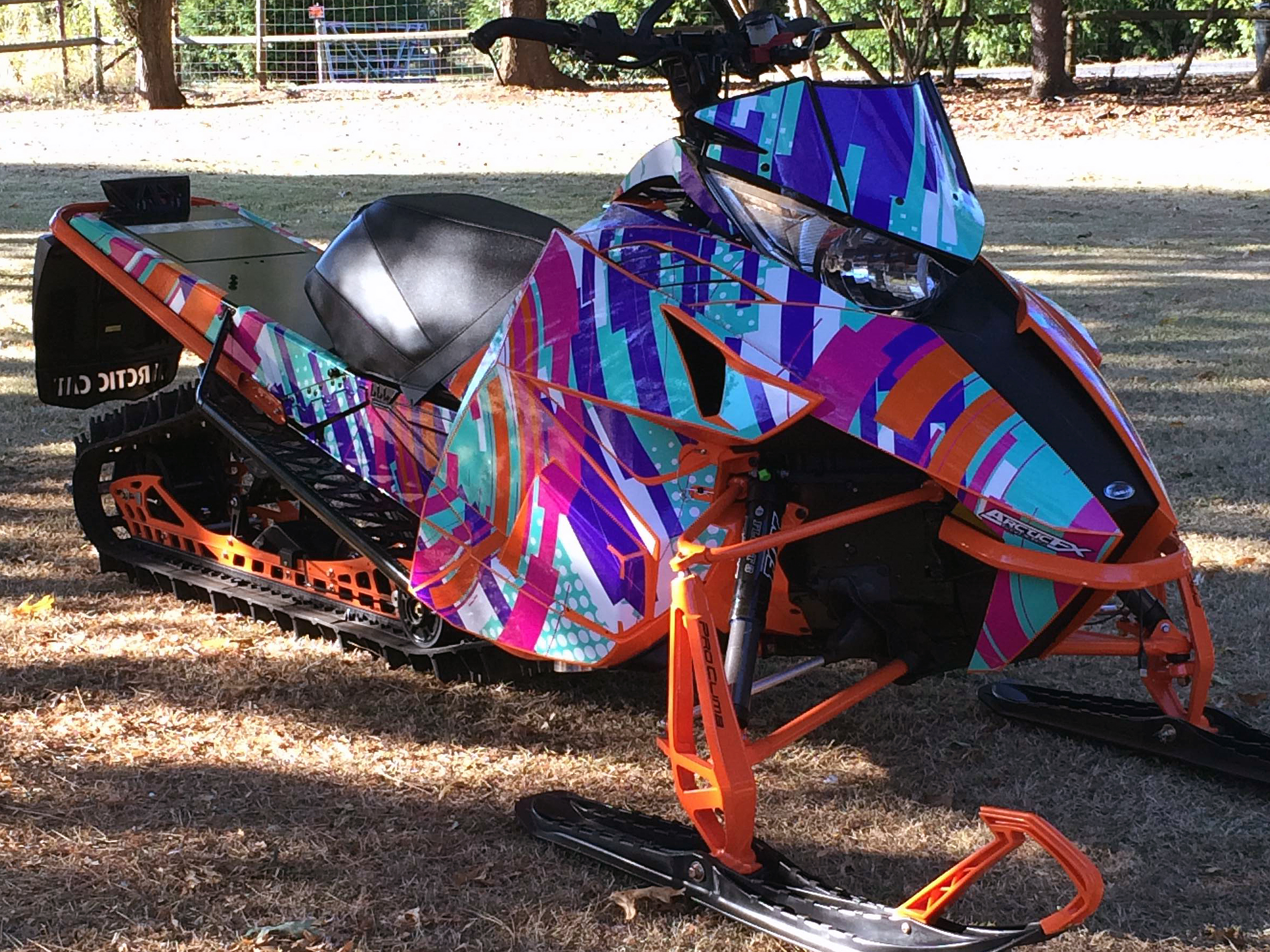 A Arctic Cat Proclimb snowmobile with a aqua, white, pink, and orange stripes Arc Reactor custom vinyl wrap.