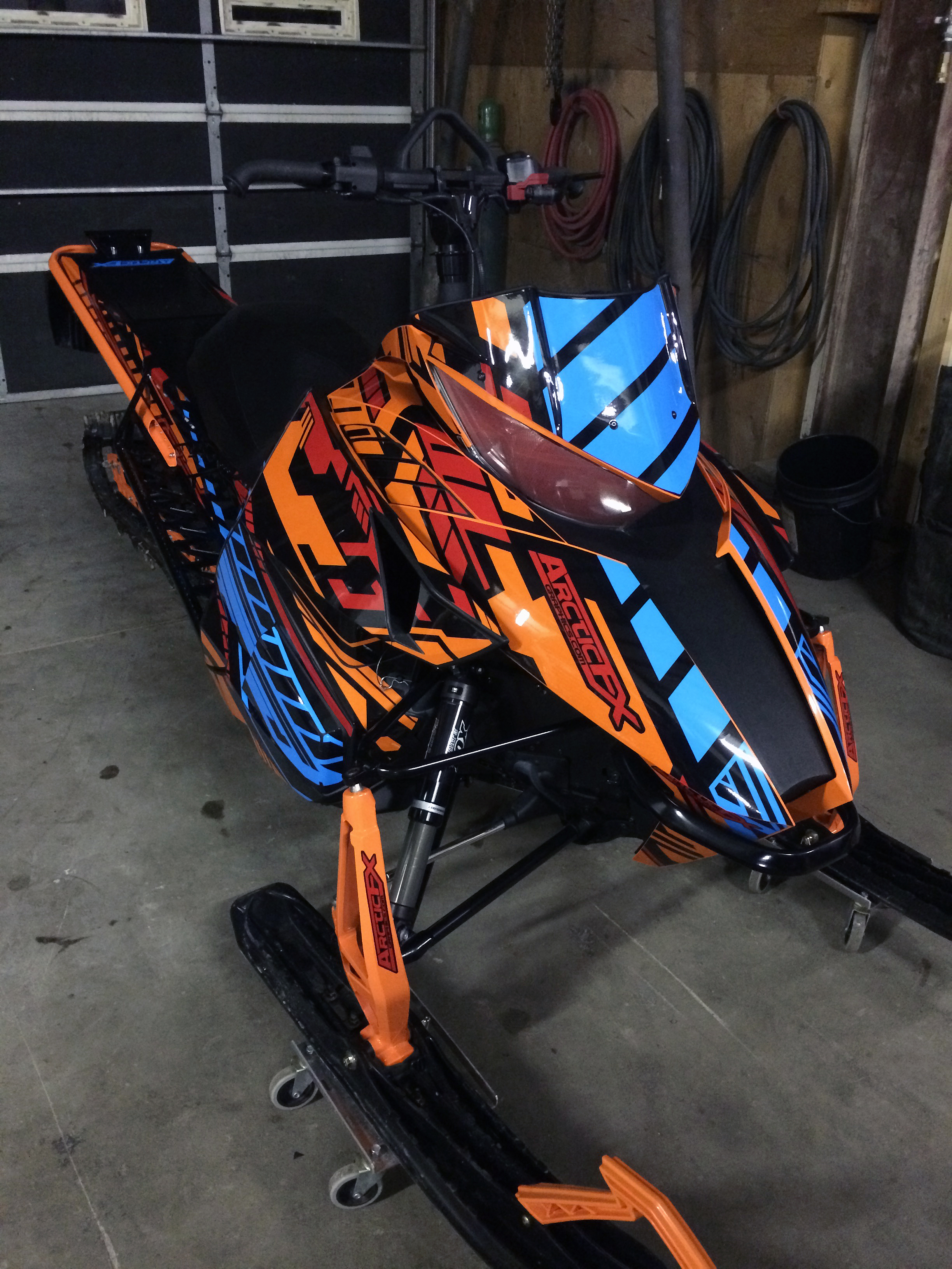 A Arctic Cat Proclimb snowmobile with a orange, black, blue and red stripes Evasion custom vinyl wrap.