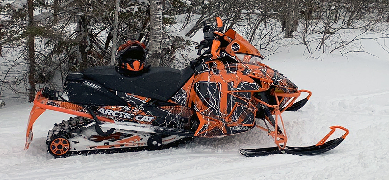 A Arctic Cat Proclimb snowmobile with a orange, white and black lightning Hard Rain custom vinyl wrap.