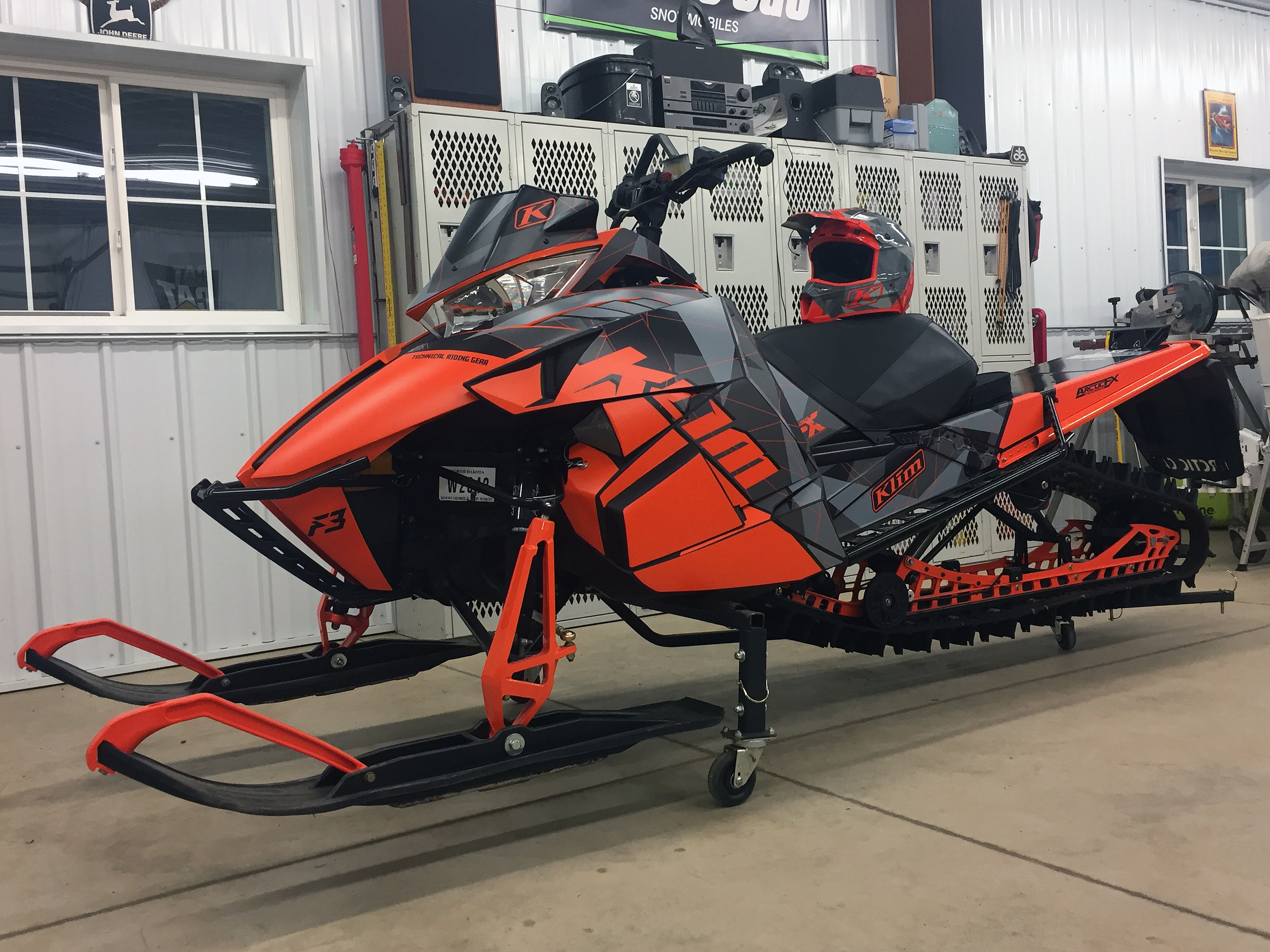 A Arctic Cat Proclimb snowmobile with a orange, gray, and black geometric Klim F3 Camo custom vinyl wrap.