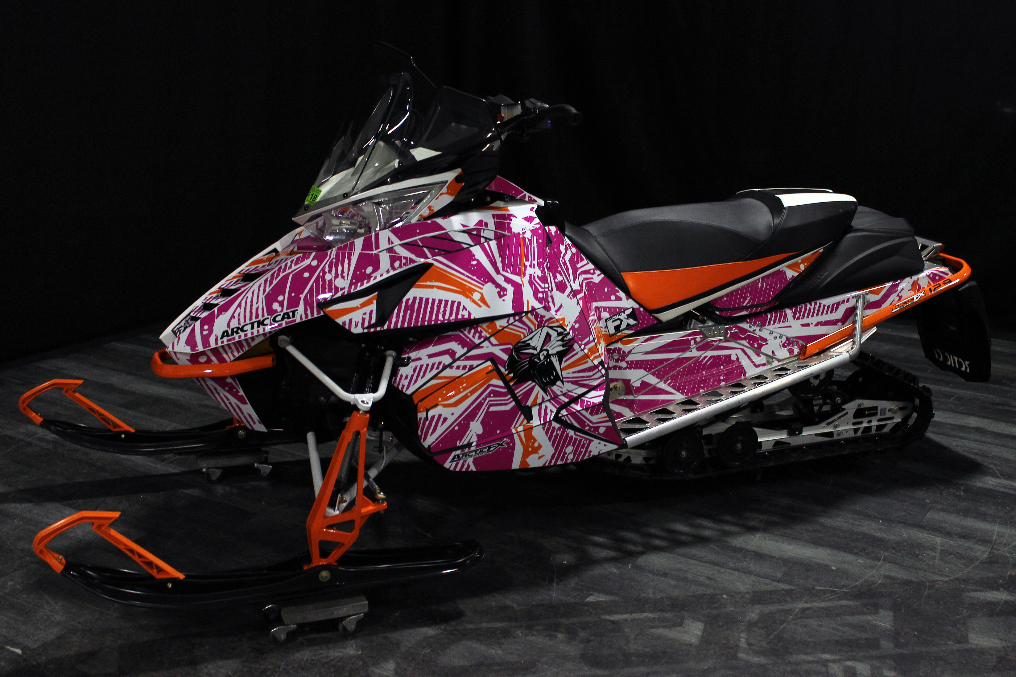 A Arctic Cat Procross snowmobile with a orange, white and pink grunge Stricken custom vinyl wrap.