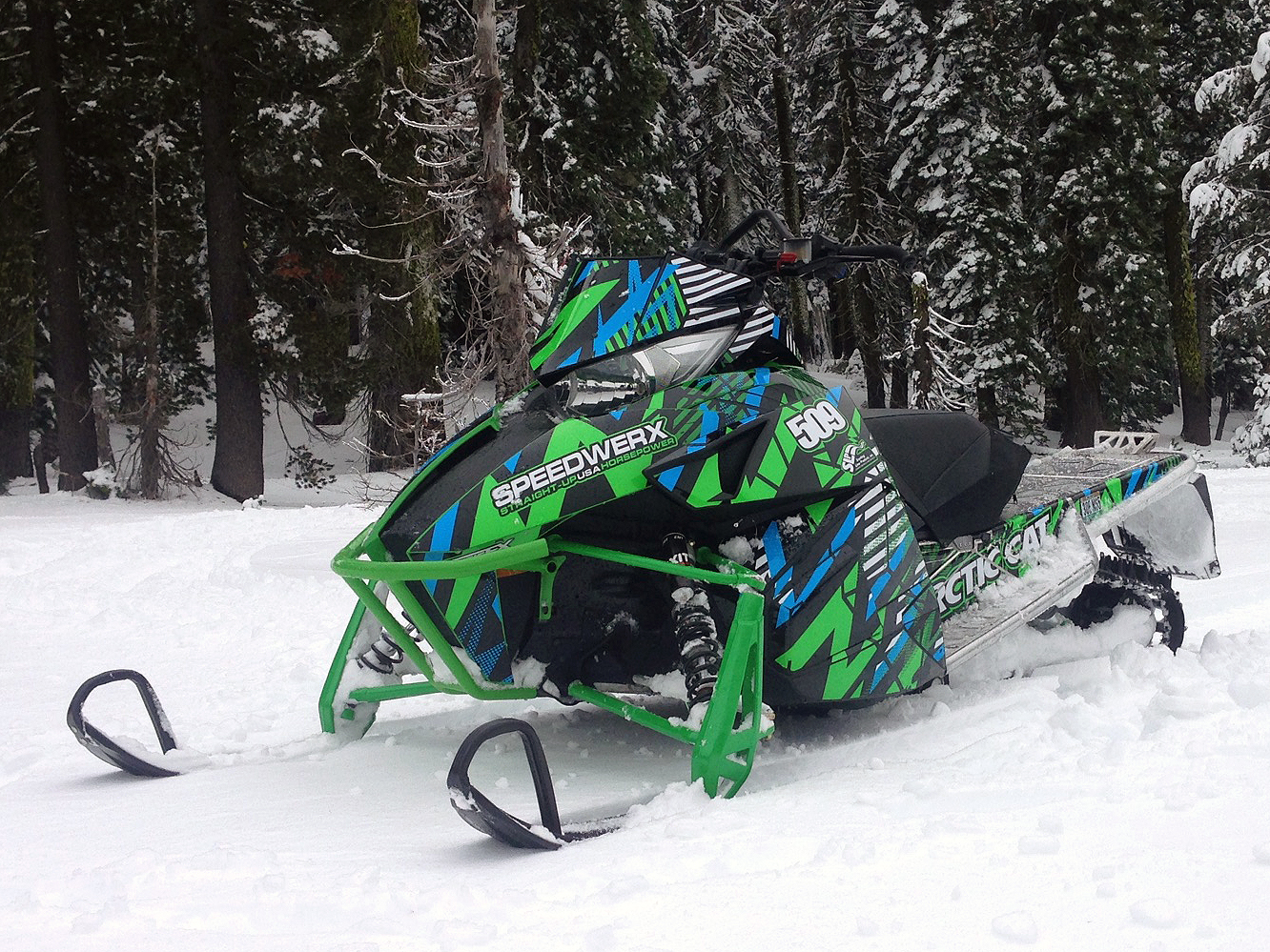 A Arctic Cat Procllimb snowmobile with a green, blue and black grunge bolt Voltage custom vinyl wrap.