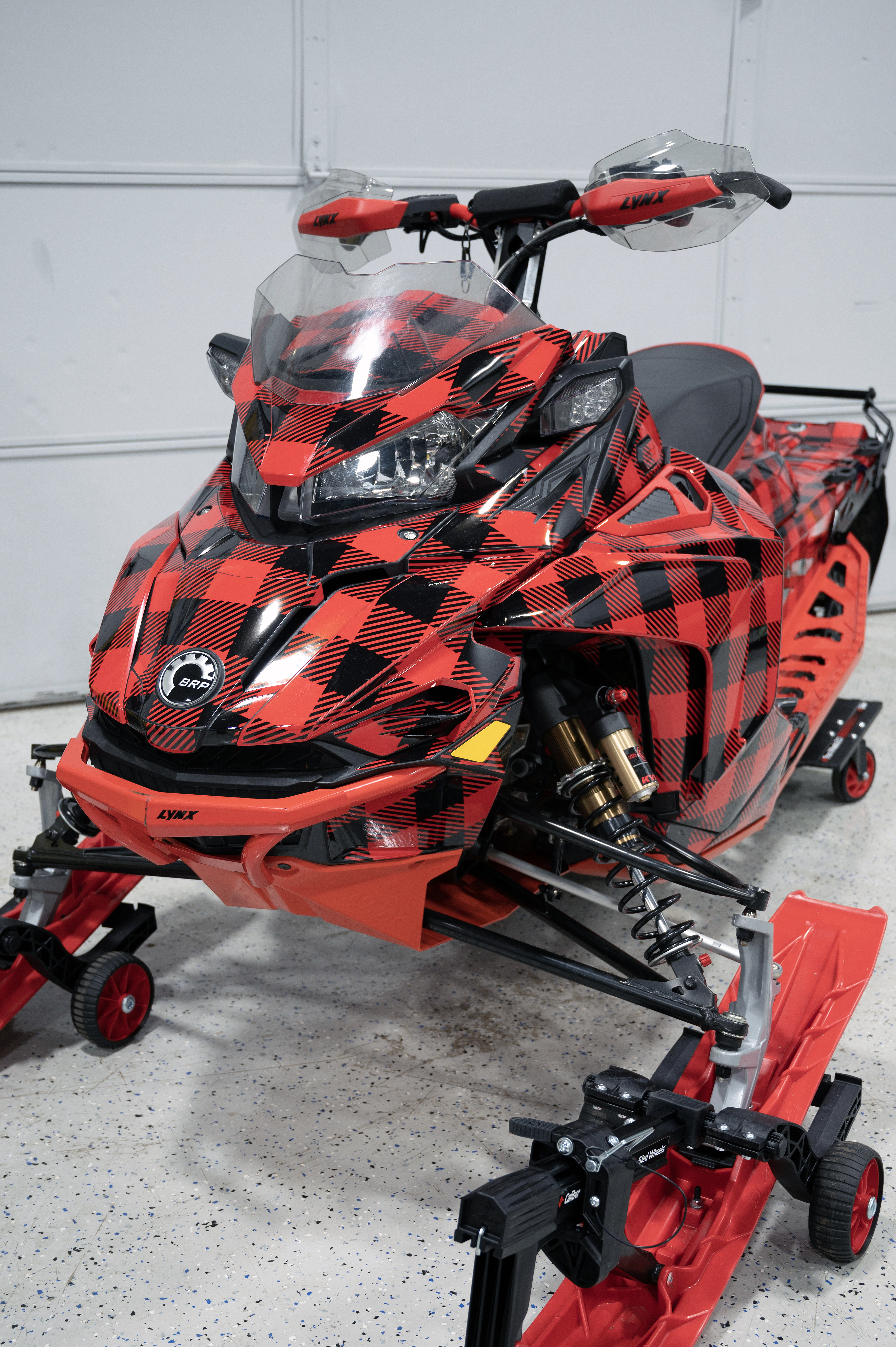 A Lynx snowmobile with a red and black Plaid pattern custom vinyl wrap with stock logos added.