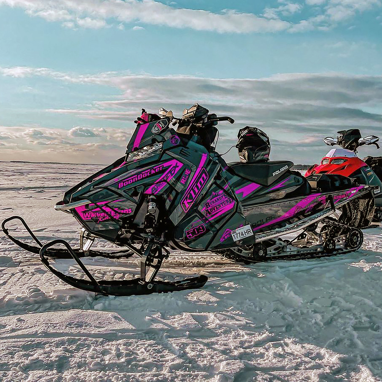 A Polaris Axys Crossover snowmobile with a pink, gray, and black stripes Burandt Evolution custom vinyl wrap.