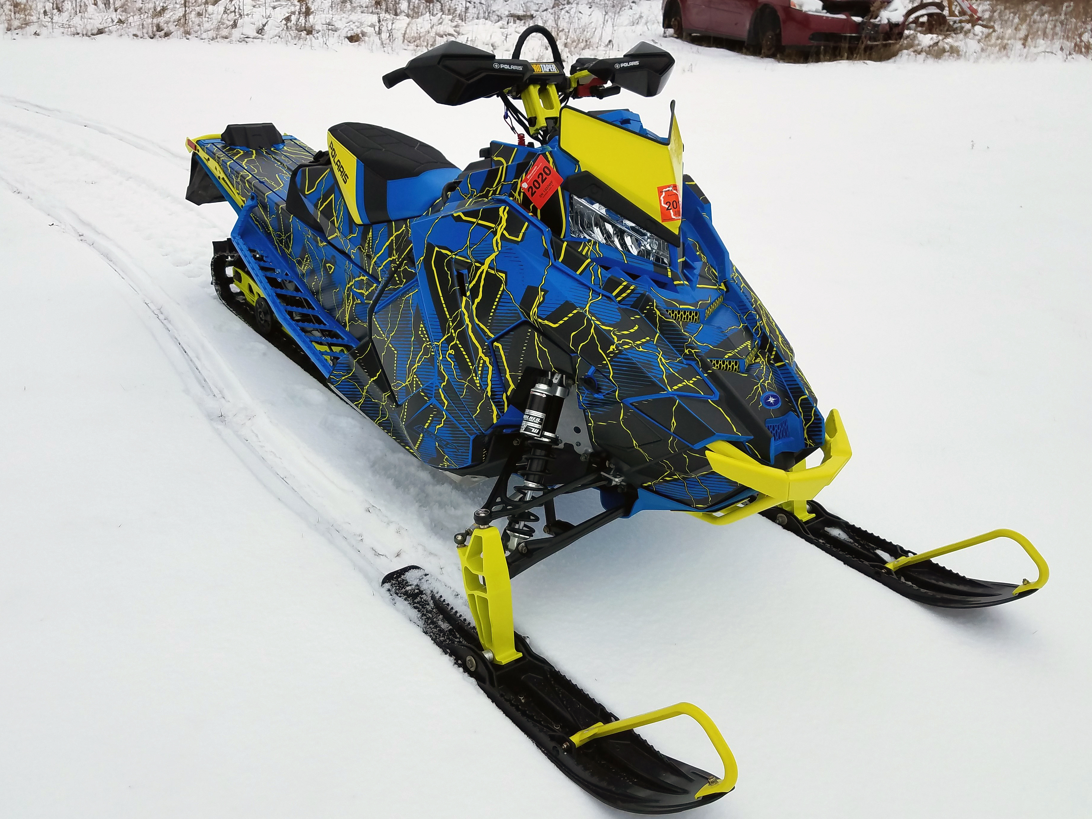 A Polaris Axys Crossover snowmobile with a lime squeeze, black, and blue lightning Hard Rain custom vinyl wrap.