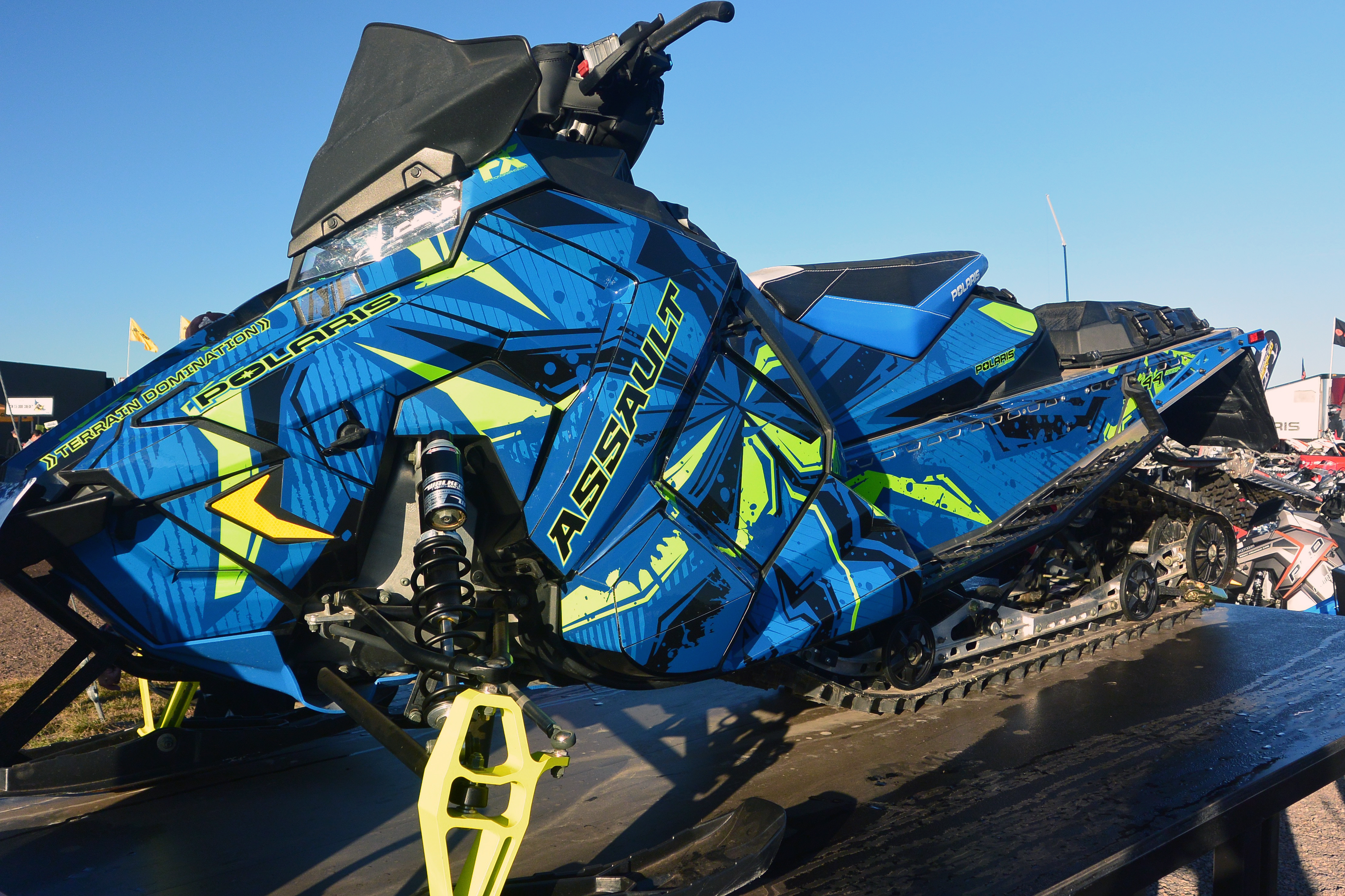 A Polaris Axys Crossover snowmobile with a lime squeeze, black, and blue Stricken custom vinyl wrap.