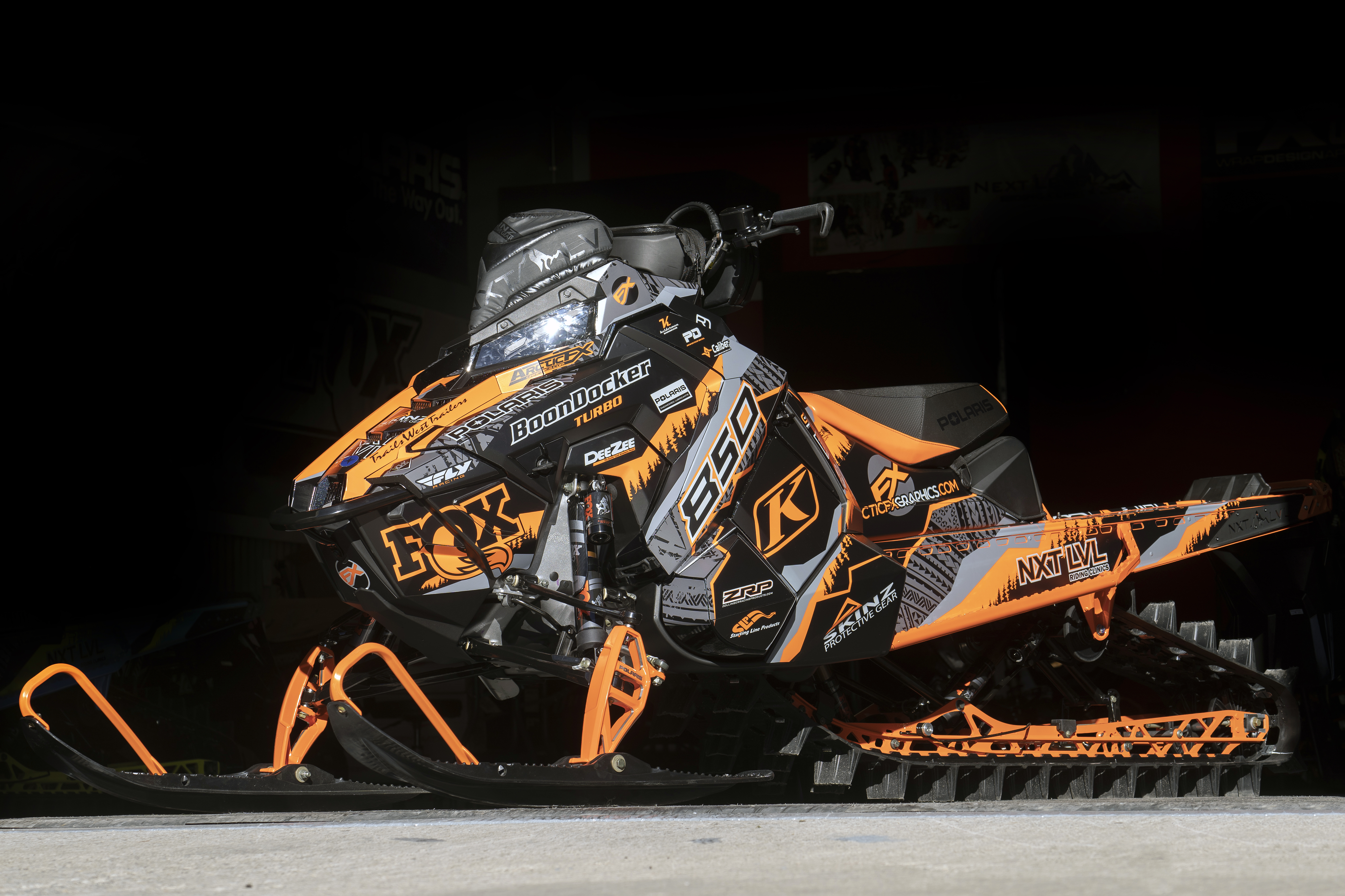 A Polaris Axys Mountain snowmobile with a orange, gray, and black tribal Adams Alpine custom vinyl wrap.