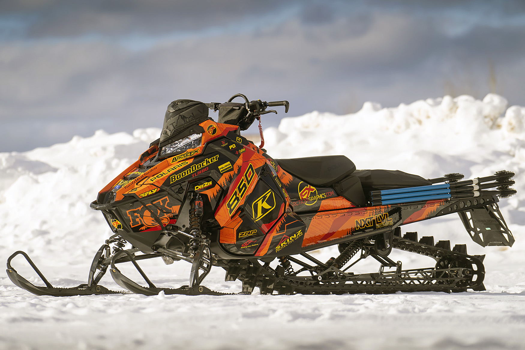 A Polaris Axys Mountain snowmobile with a red, orange, and yellow tribal Adams Alpine custom vinyl wrap.