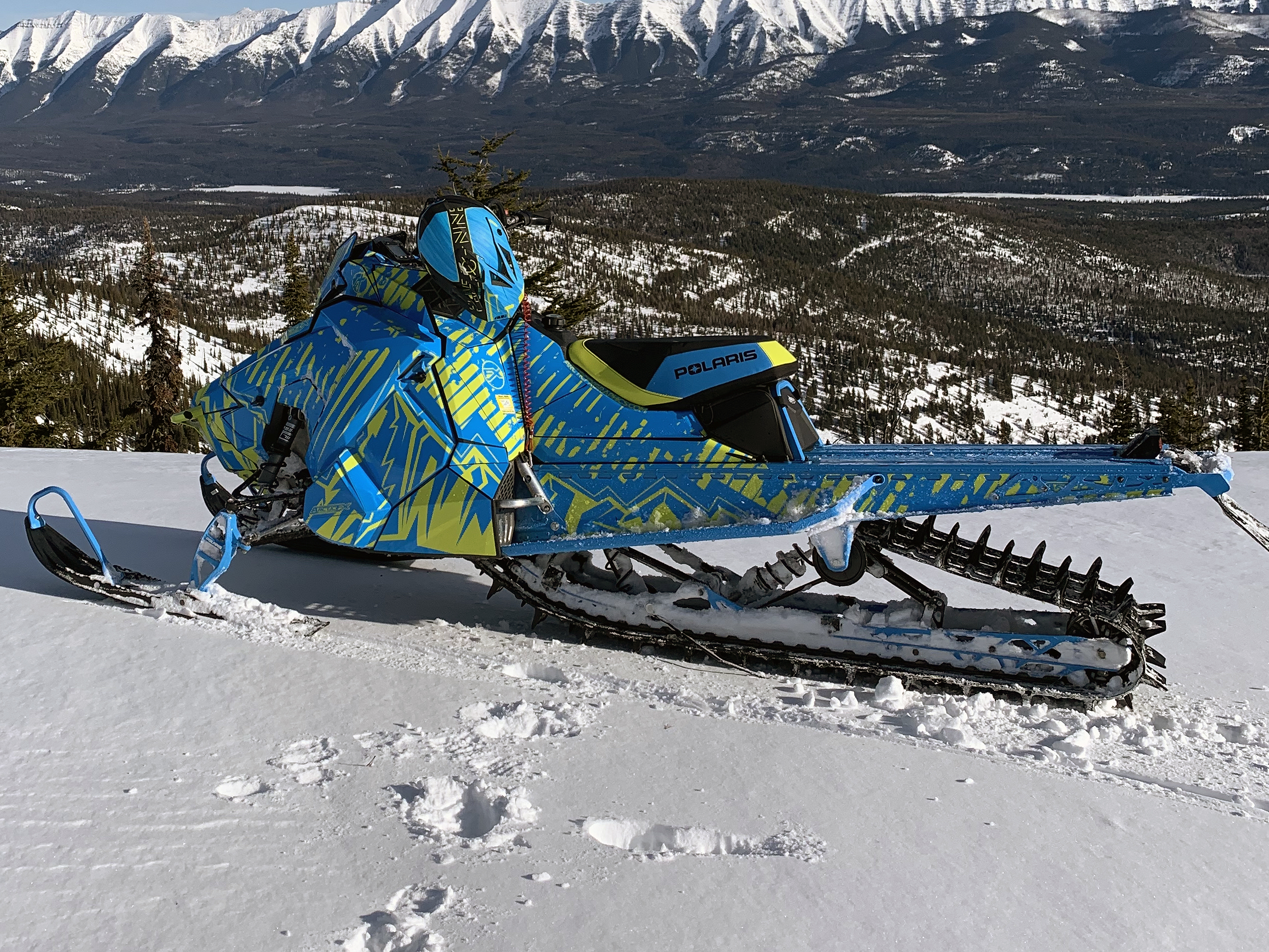A Polaris Axys Mountain snowmobile with a lime squeeze, and blue Altitude custom vinyl wrap.