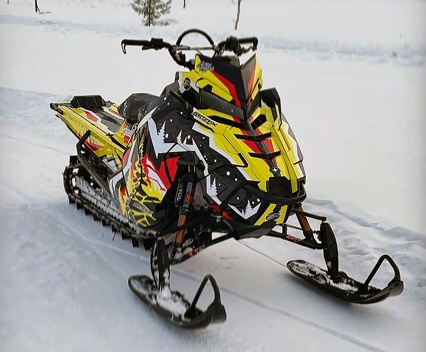 A Polaris Axys Mountain snowmobile with a yellow, red, and black Leif Alvarsson Kingdom custom vinyl wrap.
