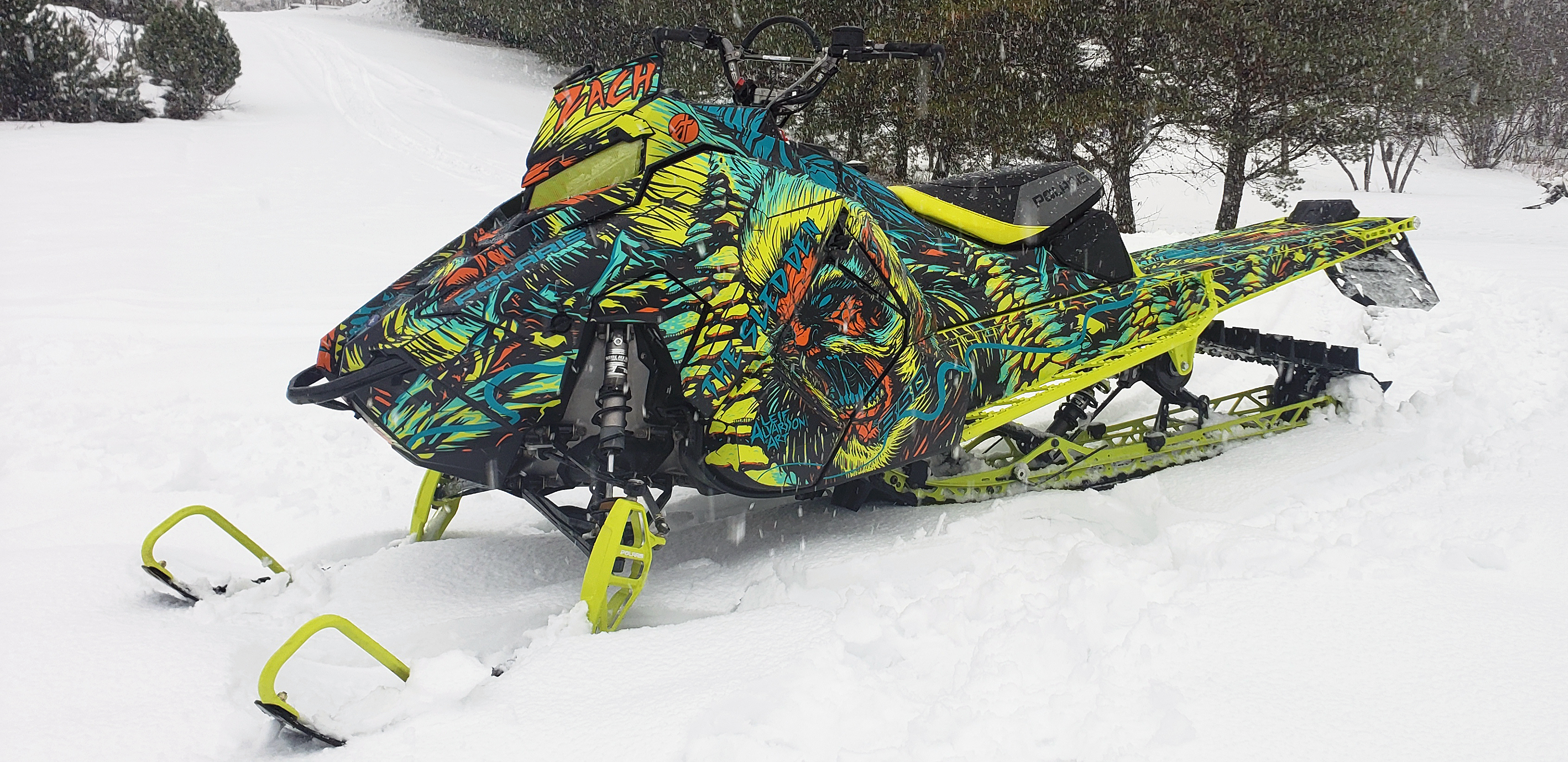 A Polaris Axys Mountain snowmobile with a lime squeeze, blue, and black Leif Alvarsson Tree Slayer custom vinyl wrap.