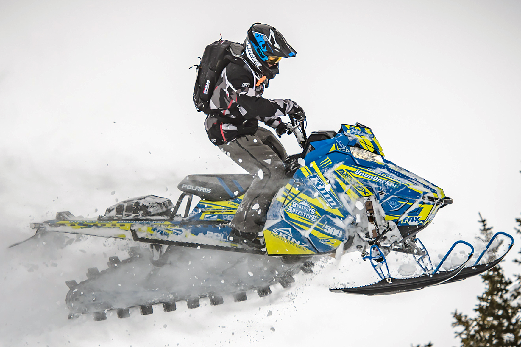 A Polaris Axys Mountain snowmobile with a yellow and blue stripes Burandt Evolution custom vinyl wrap.