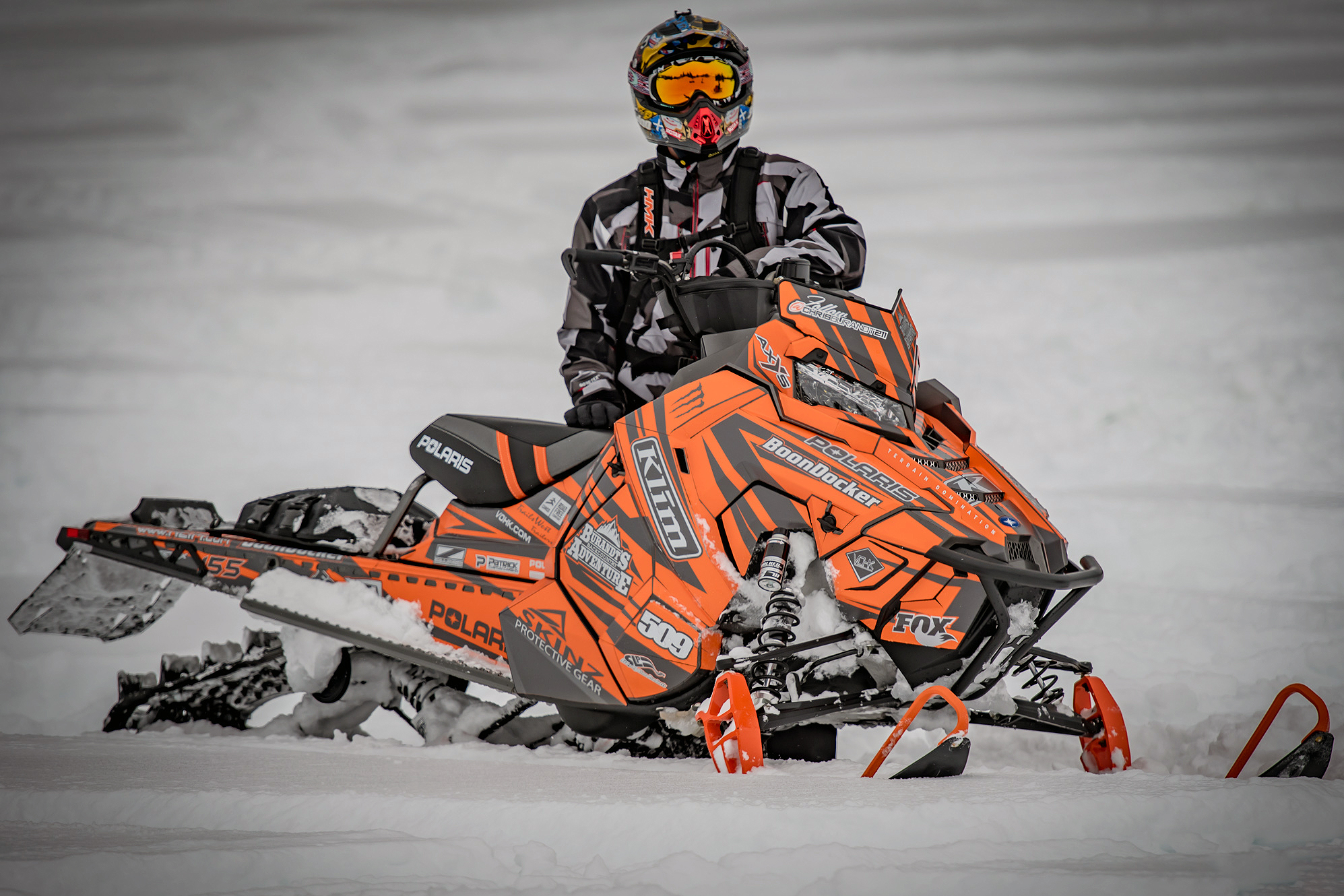 A Polaris Axys Mountain snowmobile with a orange, gray, and white stripes Burandt Evolution custom vinyl wrap.