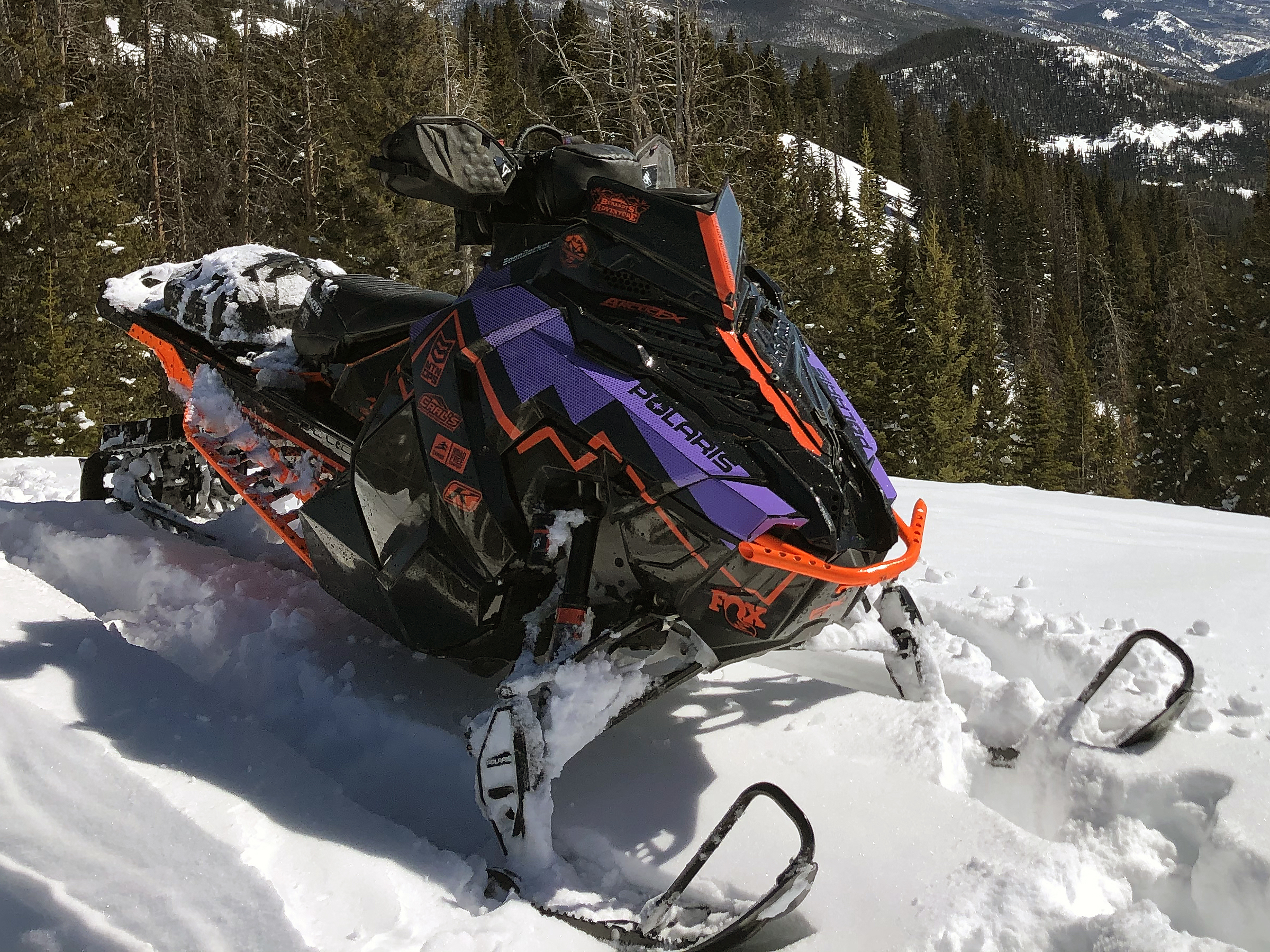 A Polaris Axys Mountain snowmobile with a orange, black, and purple Burandt Incognito custom vinyl wrap.