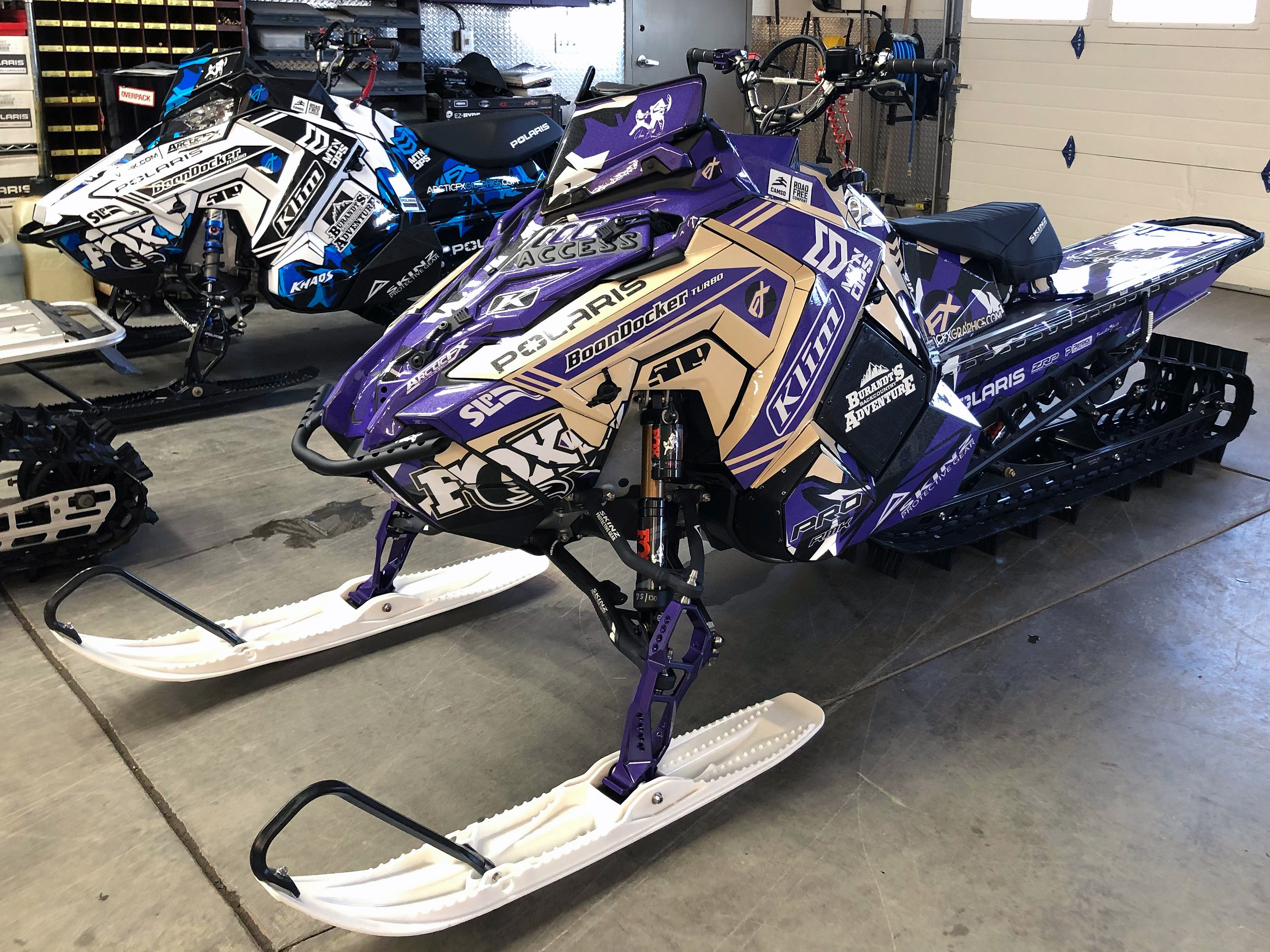A Polaris Axys Mountain snowmobile with a black, white, and purple Burandt Vista custom vinyl wrap.