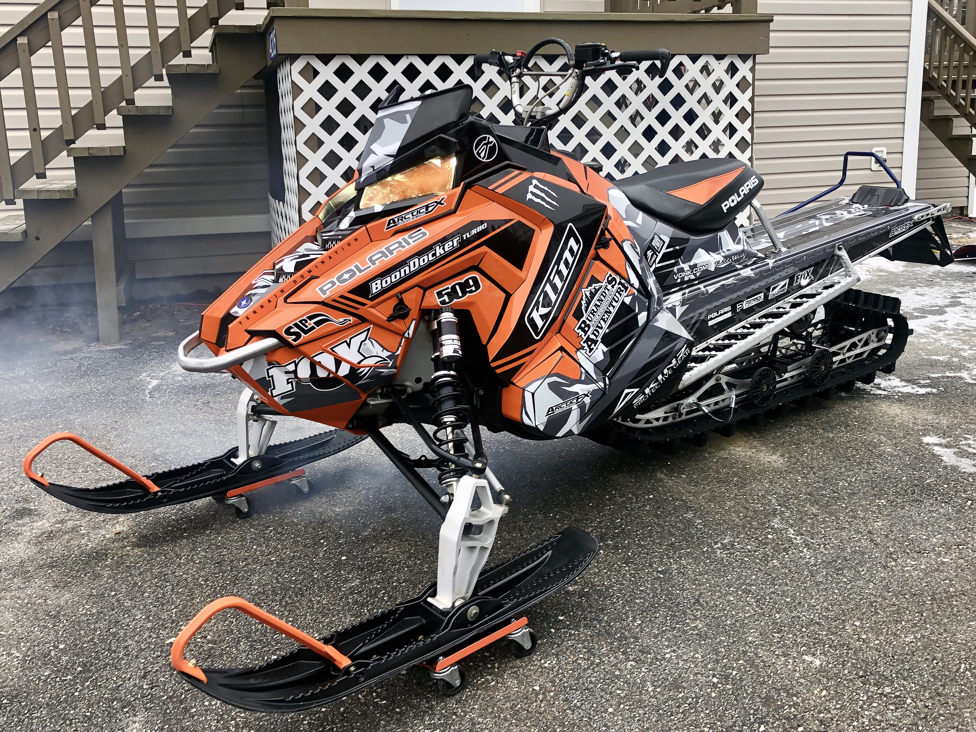 A Polaris Axys Mountain snowmobile with a black, orange, and white Burandt Vista custom vinyl wrap.