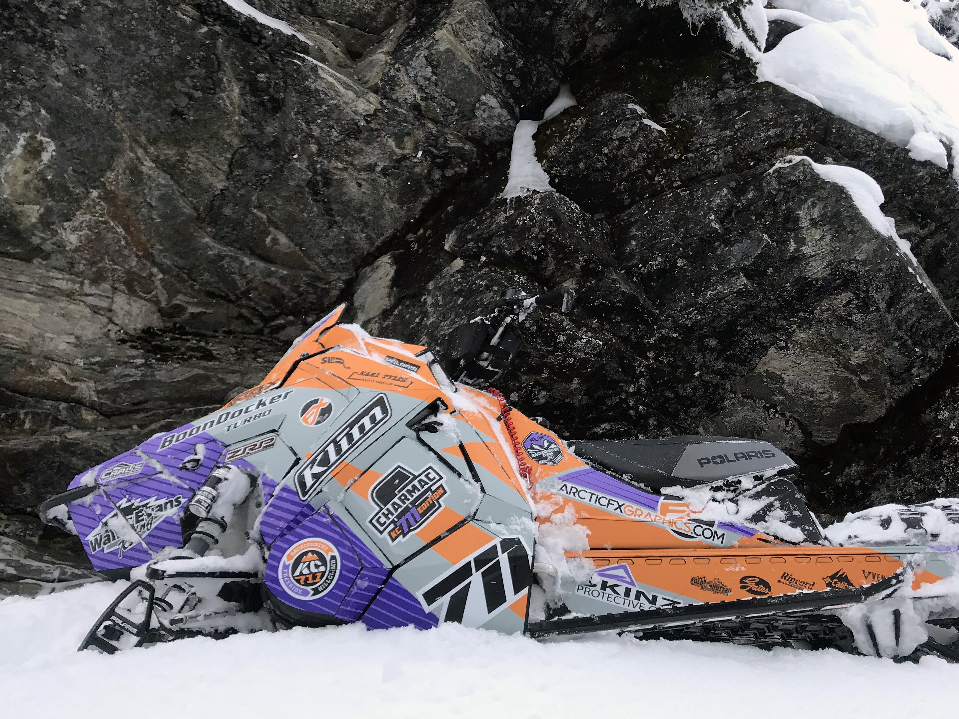 A Polaris Axys Mountain snowmobile with a orange, purple, and gray Curtis Ascent custom vinyl wrap.