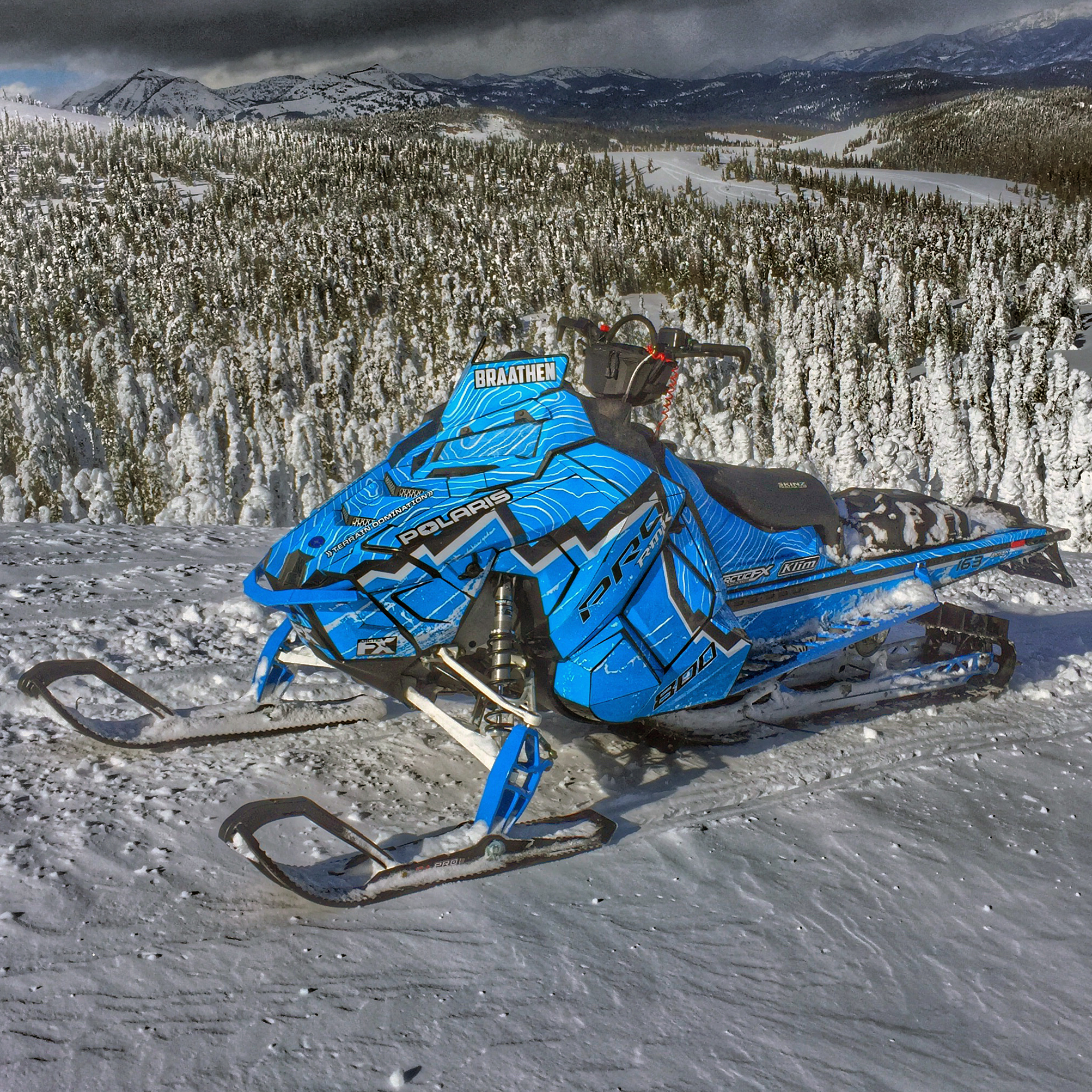 A Polaris Axys Mountain snowmobile with a blue, gray, and white Entz Frontier custom vinyl wrap.
