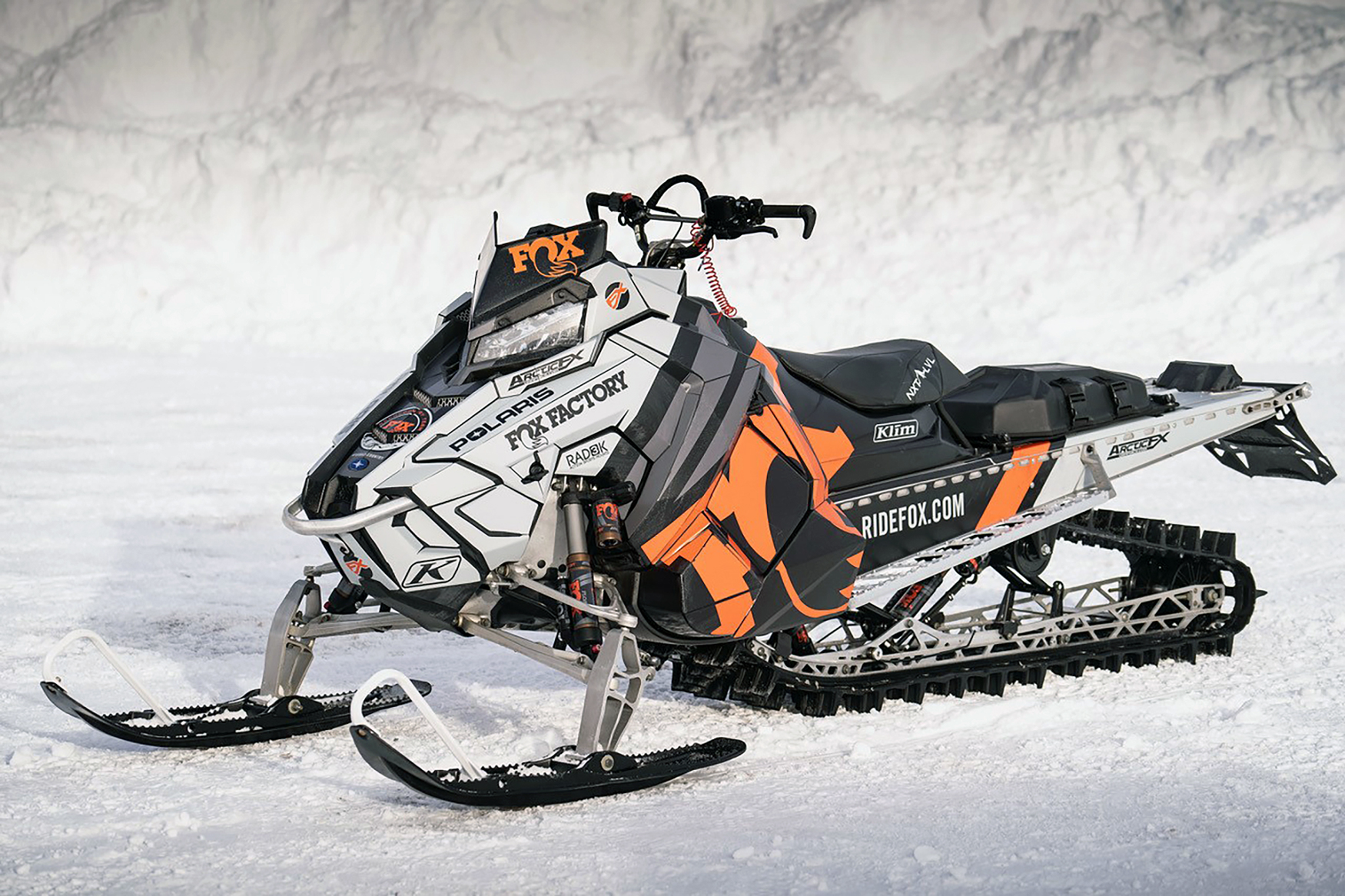 Two Polaris Axys Mountain snowmobiles with a white, gray, black, and orange Fox Rebound custom vinyl wraps.