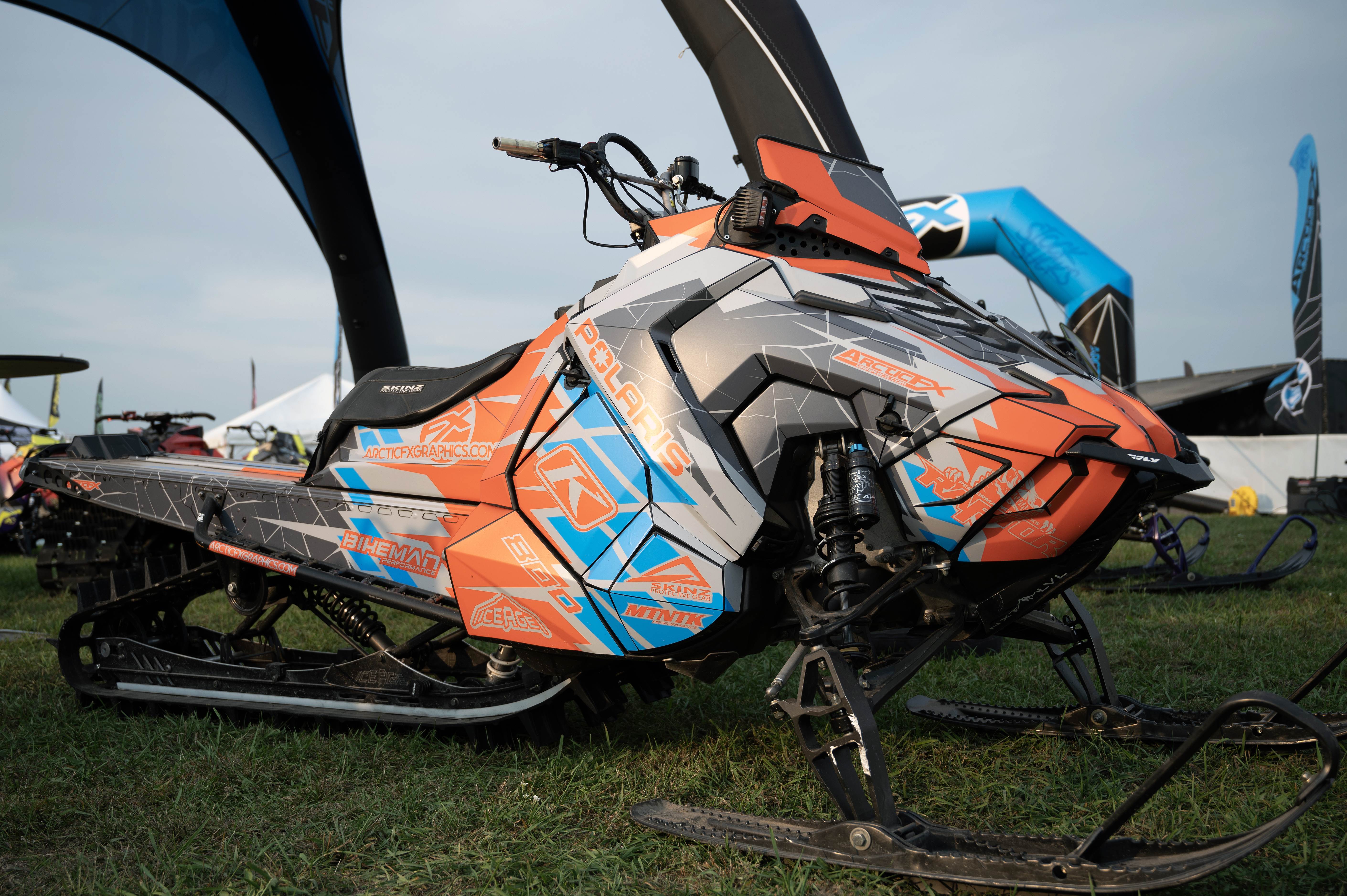 A Polaris Axys Mountain snowmobile with a gray, blue, and orange Frostbite custom vinyl wrap.
