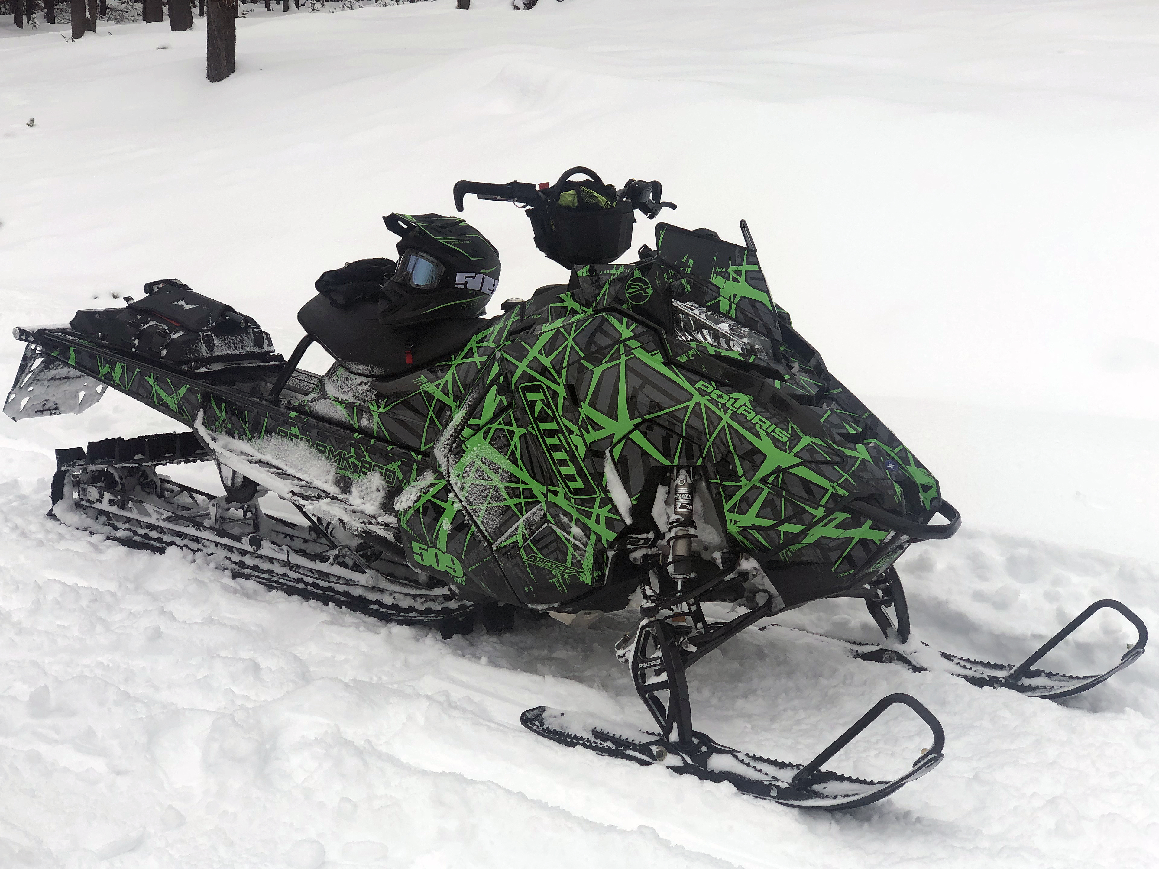 A Polaris Axys Mountain snowmobile with a green, gray, and black Ice Breaker Custom custom vinyl wrap.