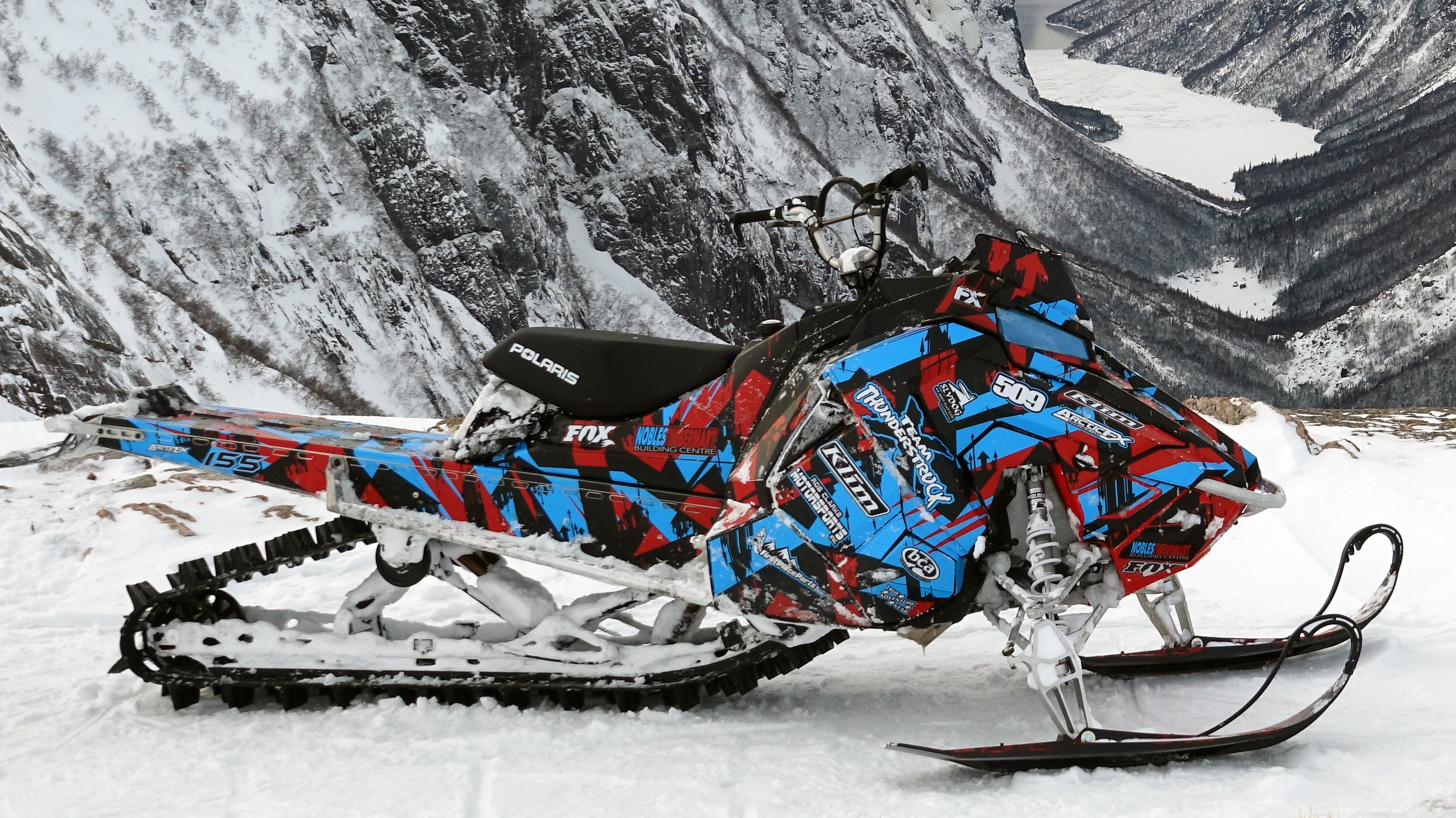 A Polaris Axys Mountain snowmobile with a red, black, and blue arrows Insidious custom vinyl wrap.