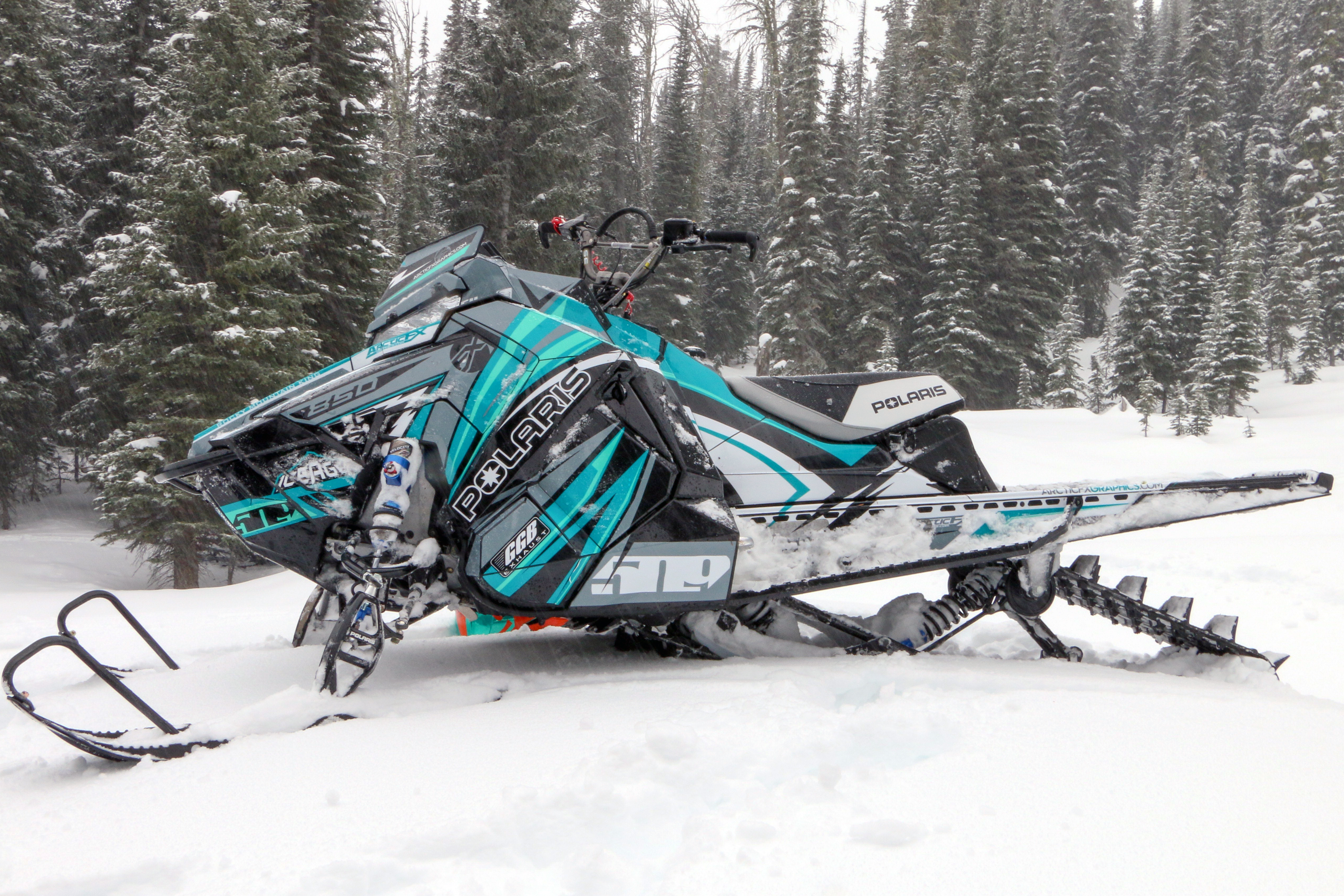 A Polaris Axys Mountain snowmobile with a teal, black, and white Kesterke Adrenaline custom vinyl wrap.