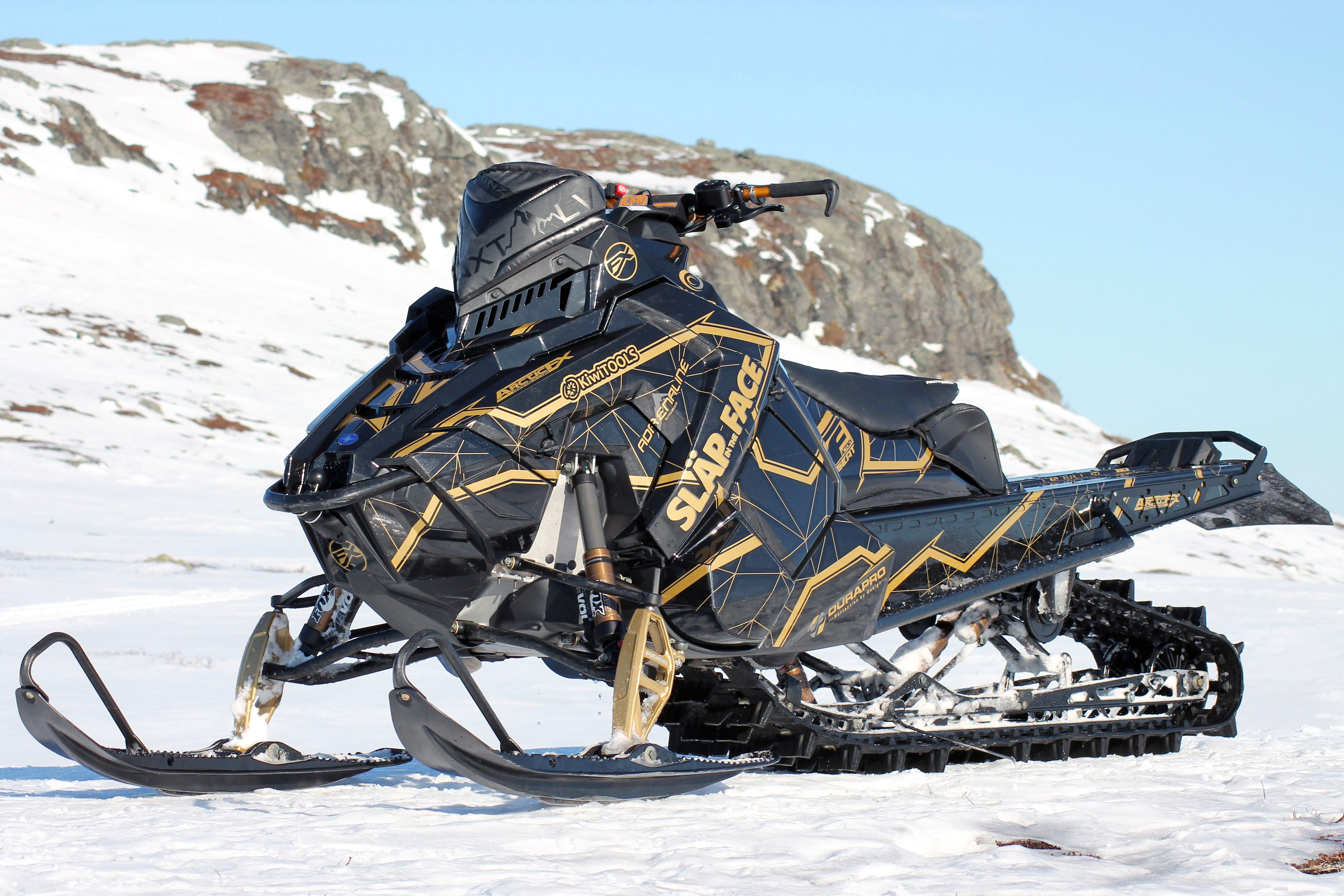 A Polaris Axys Mountain snowmobile with a black and gold Klim Demolish custom vinyl wrap.