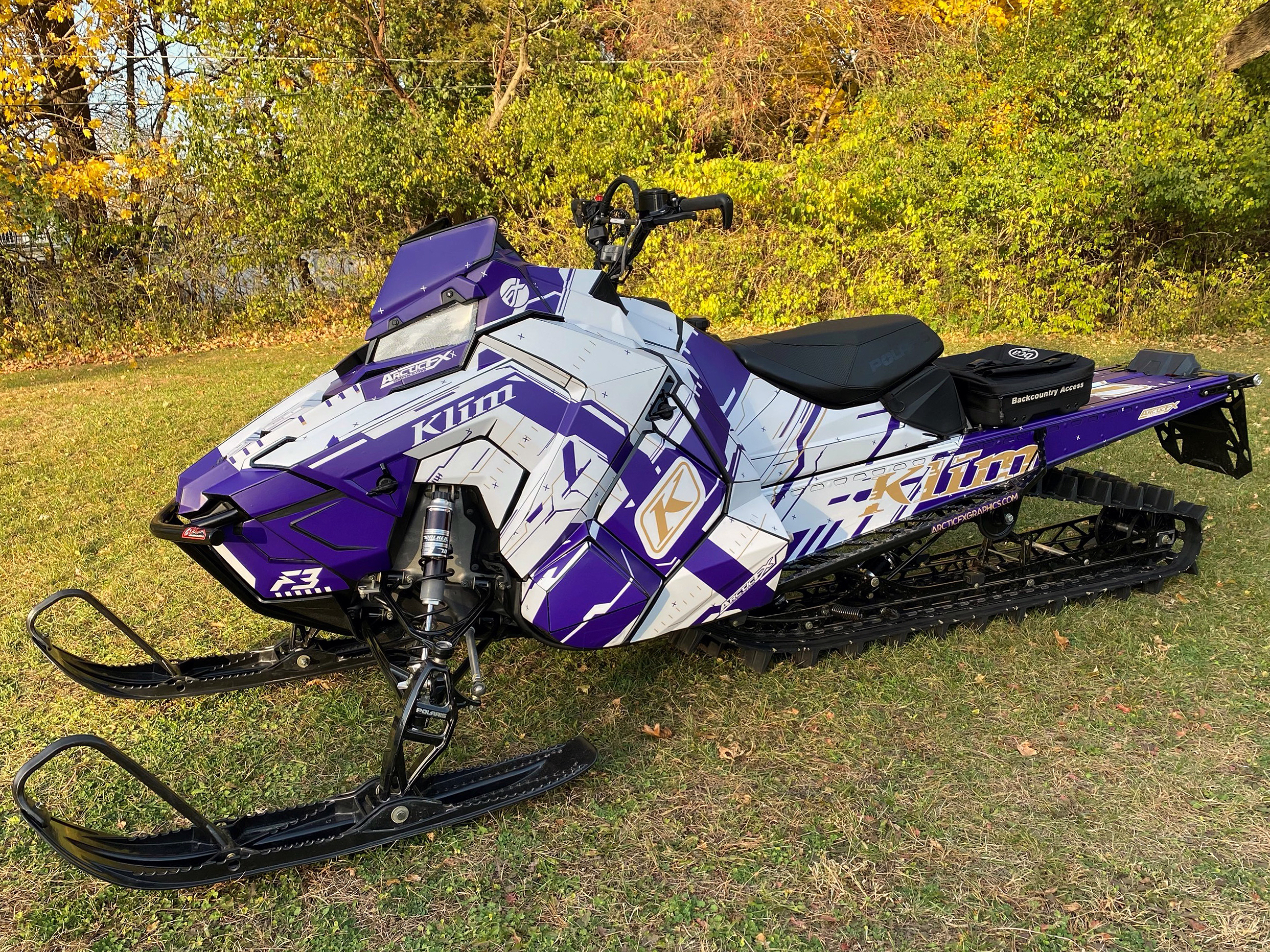 A Polaris Axys Mountain snowmobile with a purple and white Klim Recoil custom vinyl wrap.