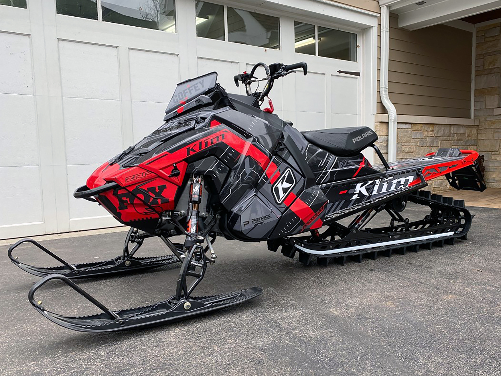 A Polaris Axys Mountain snowmobile with a black, red, and gray Klim Recoil custom vinyl wrap.