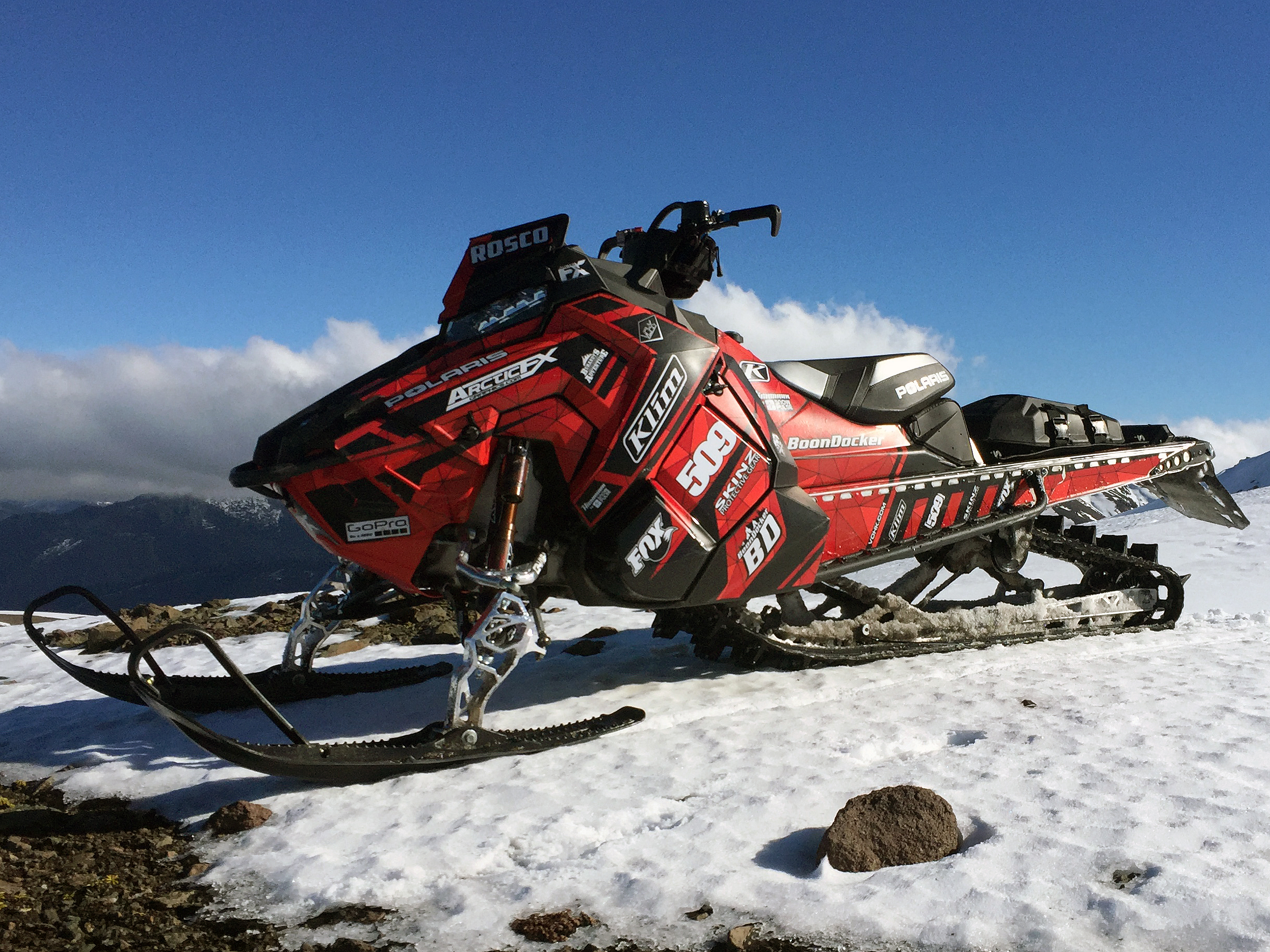 A Polaris Axys Mountain snowmobile with a red, black, and white Minerva custom vinyl wrap.